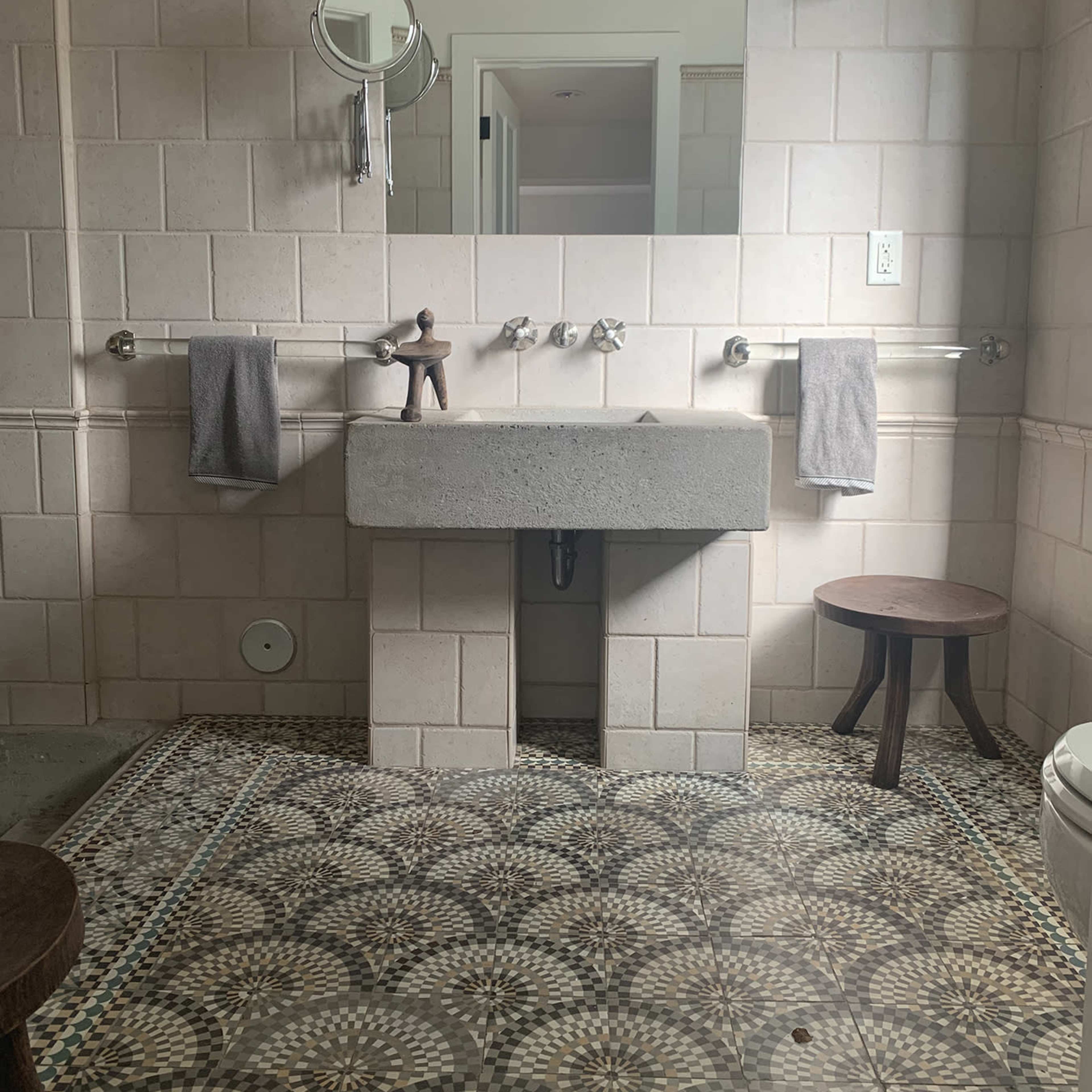 A bathroom with a concrete sink, wall-mounted mirrors, two light fixtures, and a patterned floor.