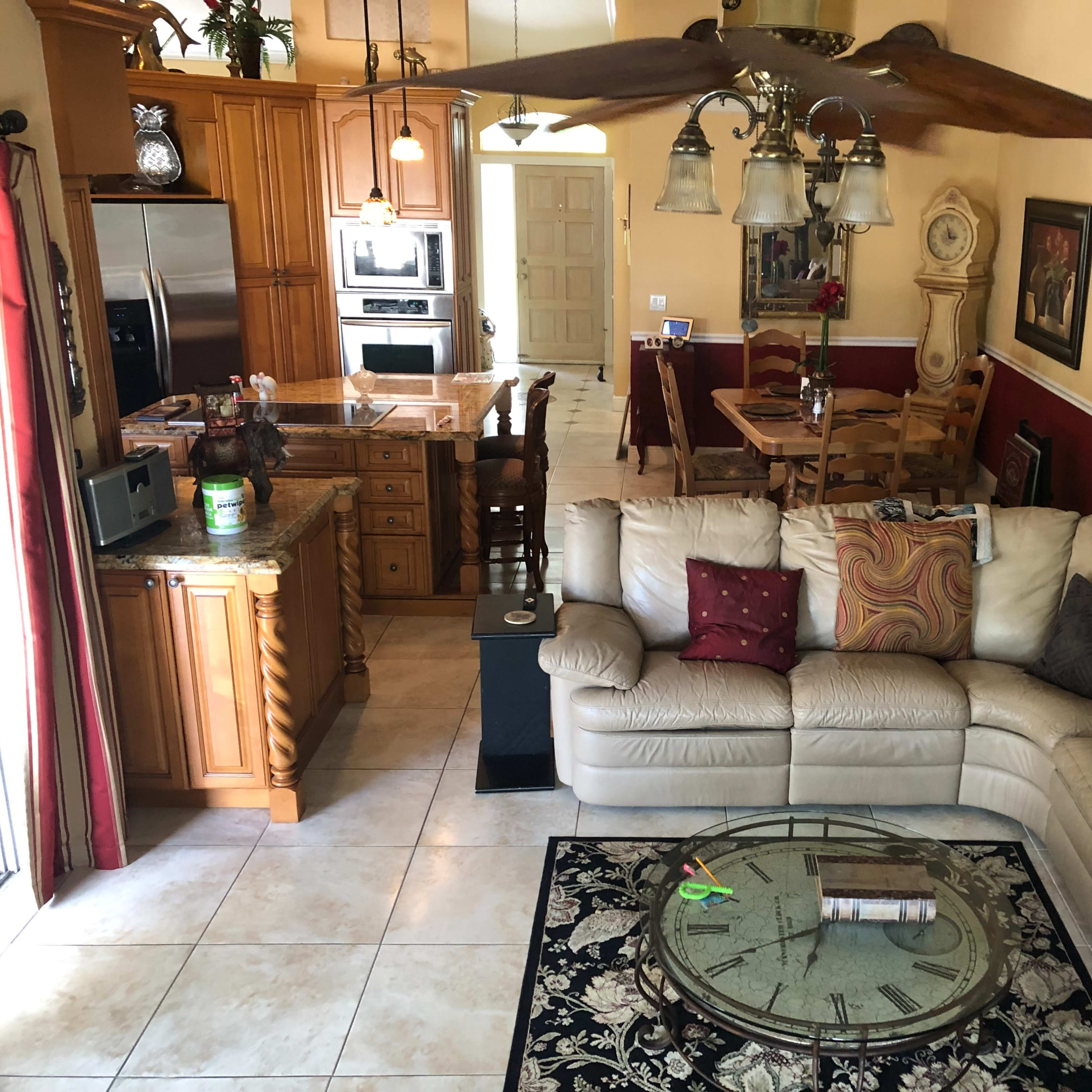 A spacious living area featuring a beige sectional sofa, a round coffee table with magazines, and a dining area with a wooden table and chairs against a backdrop of warm-colored walls.