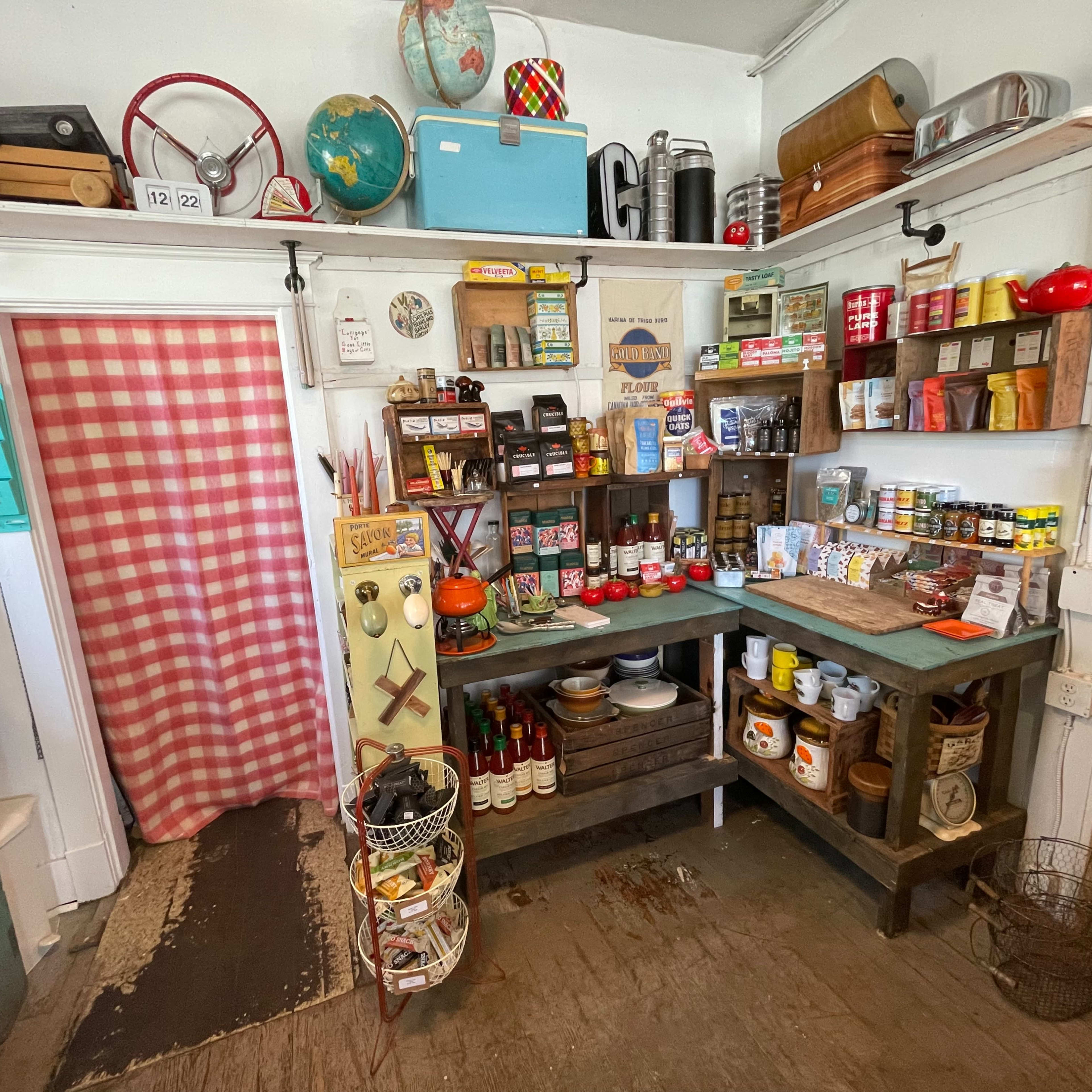 A vintage-style kitchen pantry filled with an assortment of canned goods, jars, and kitchen tools, arranged on wooden shelves.