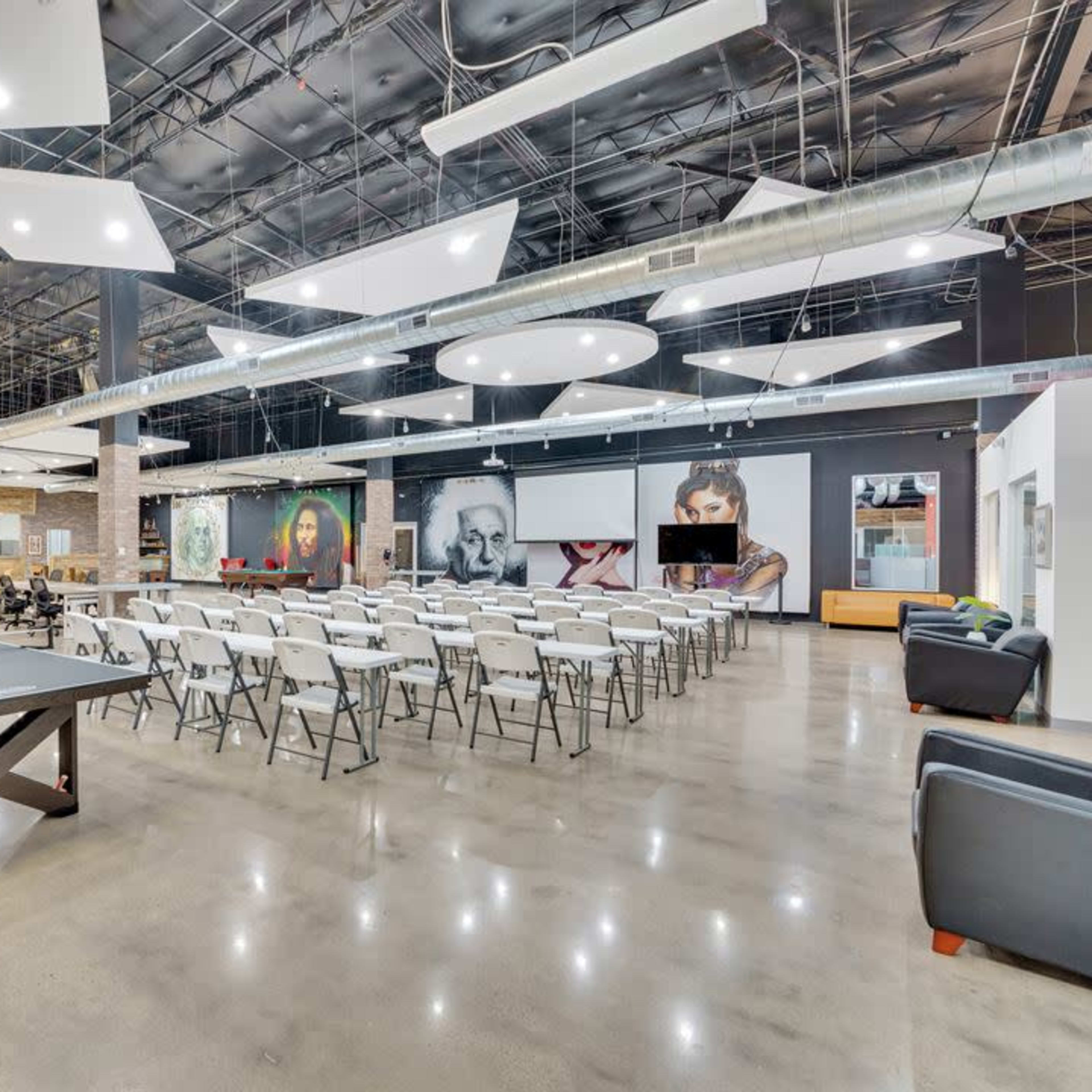 A spacious indoor venue with folding chairs arranged in rows, a ping pong table, and large wall art in a well-lit environment.