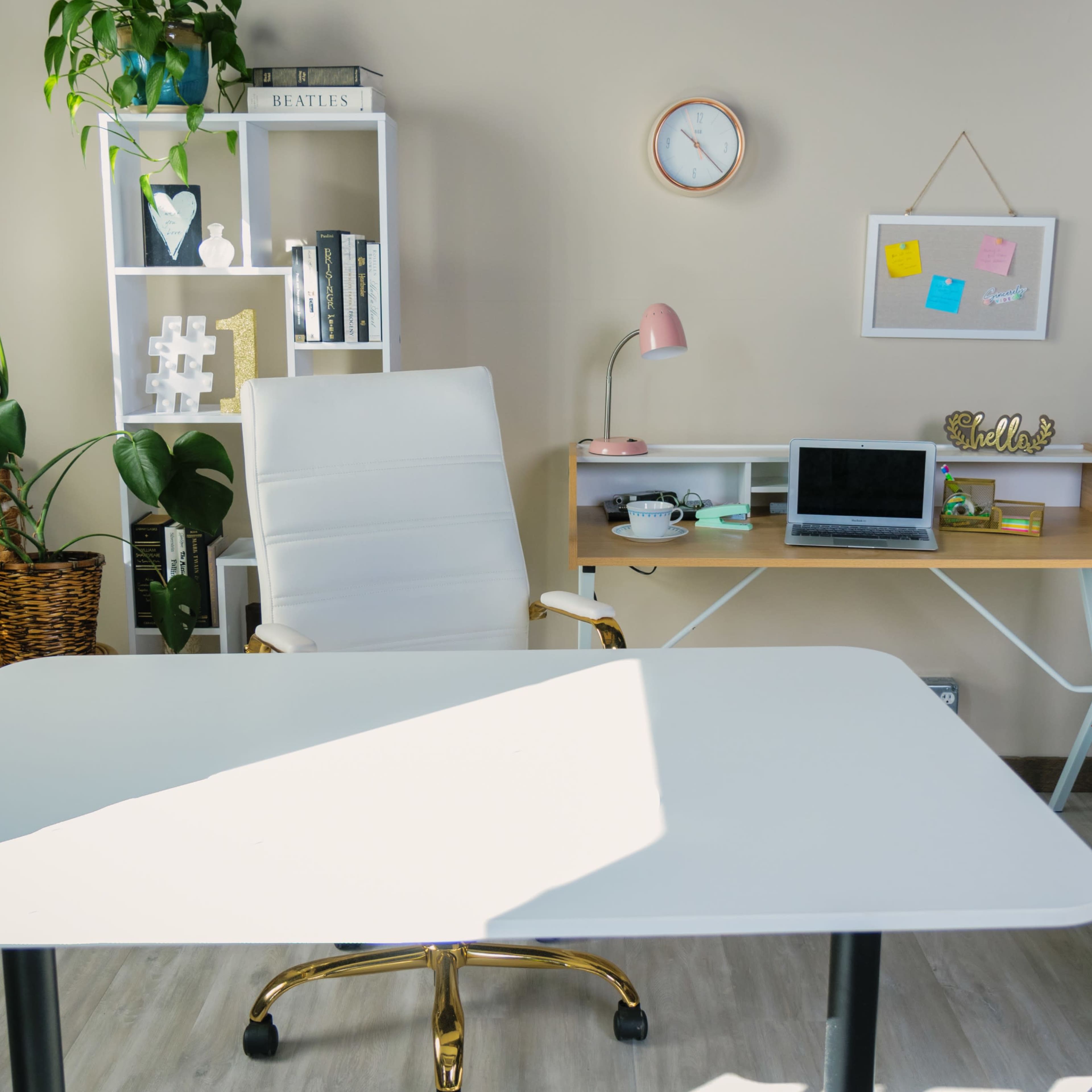A modern office space featuring a white desk, a swivel chair, a laptop on a wooden desk, and various plants in the background.