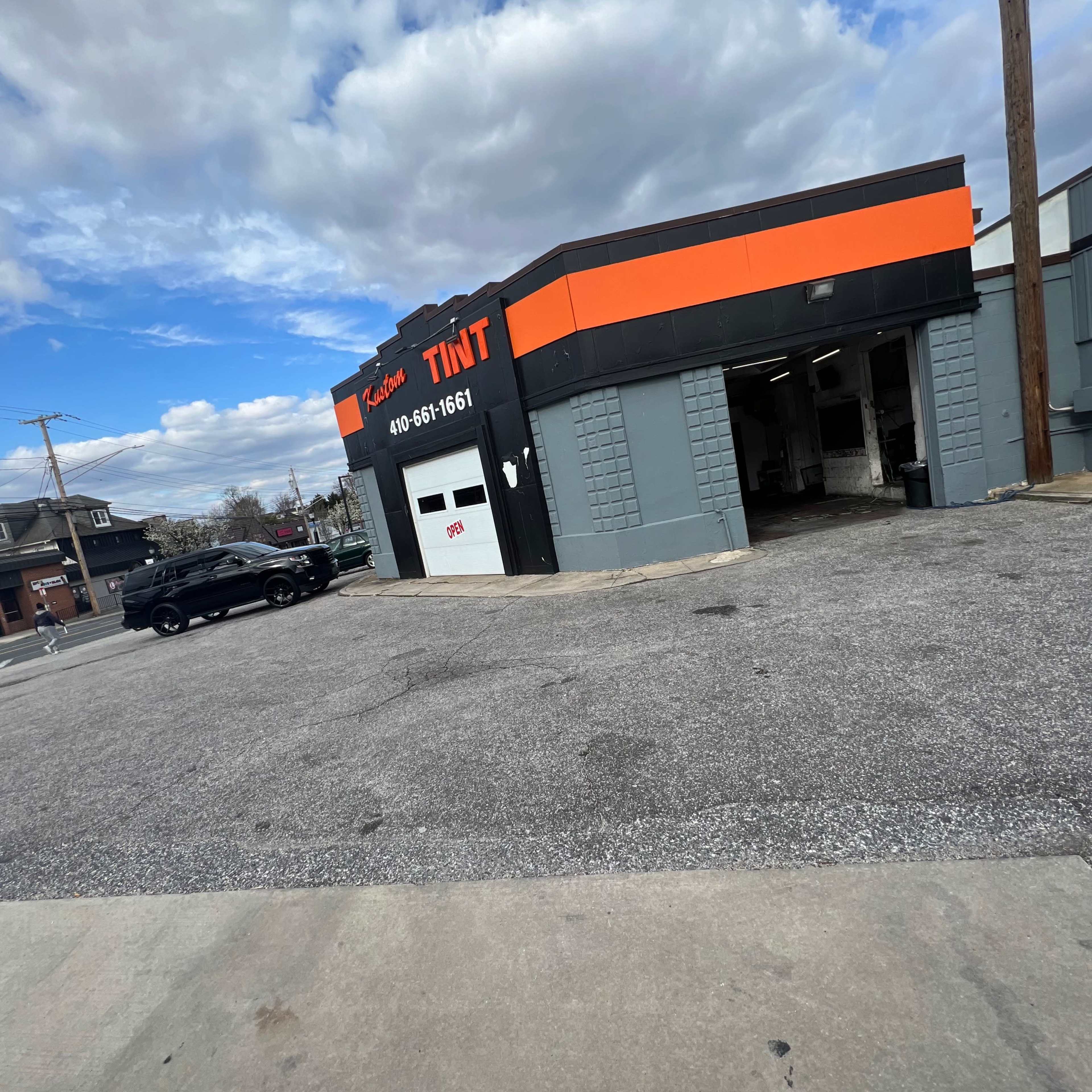 A tinting shop with a black car parked in front, set against a backdrop of cloudy skies.