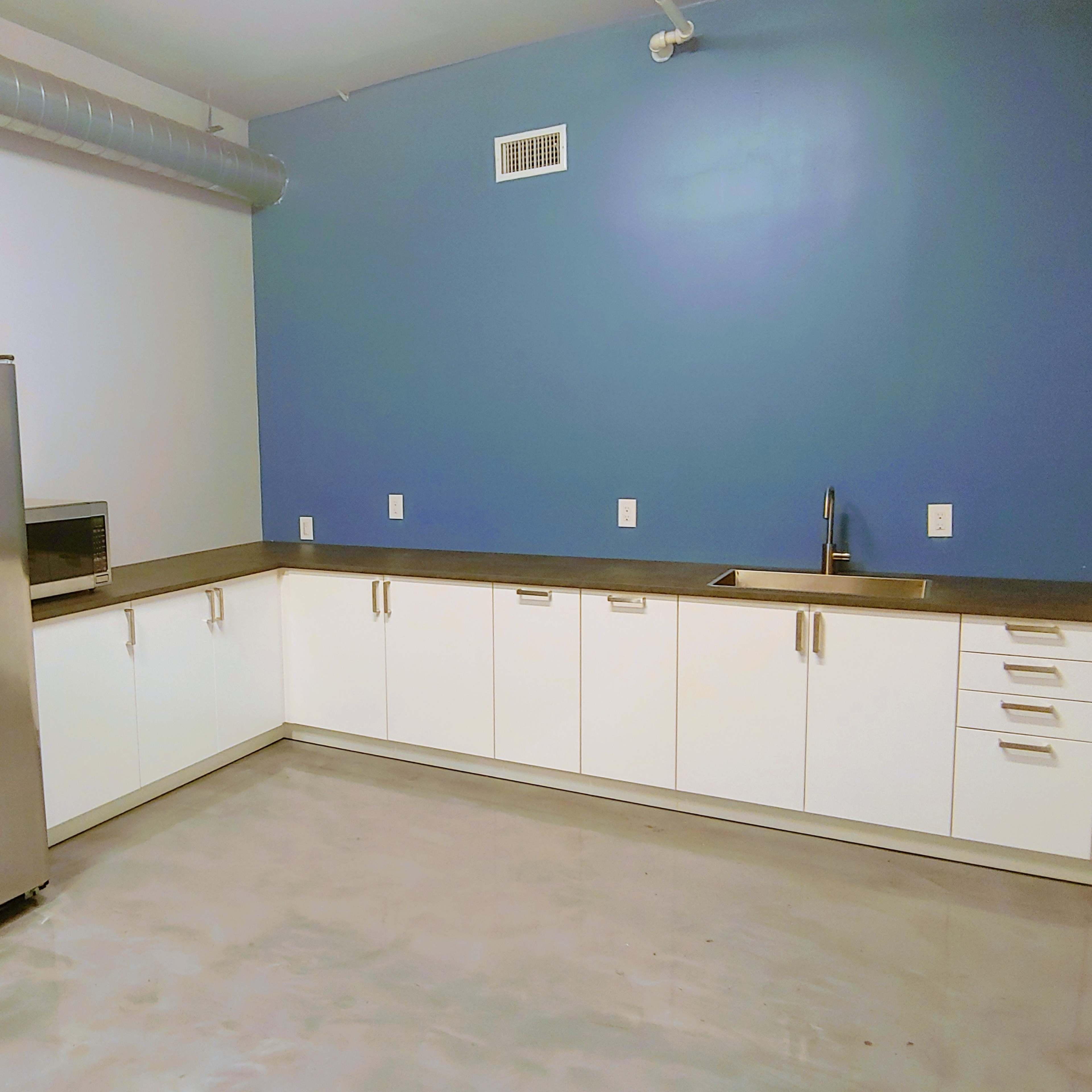 A modern kitchen with stainless steel appliances, white cabinetry, a blue accent wall, and a concrete floor.