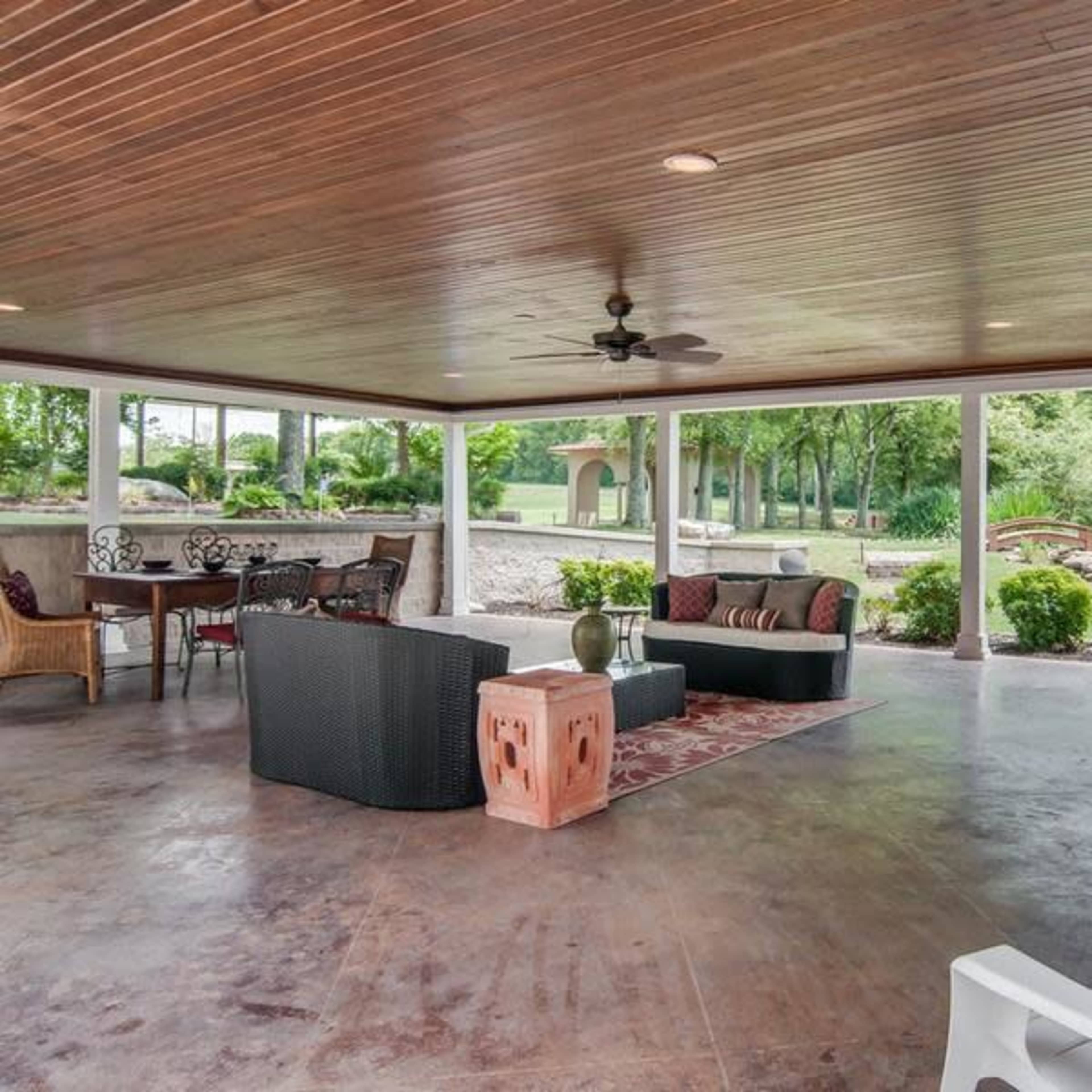 A spacious covered patio with various seating arrangements, a ceiling fan, and views of a landscaped garden.