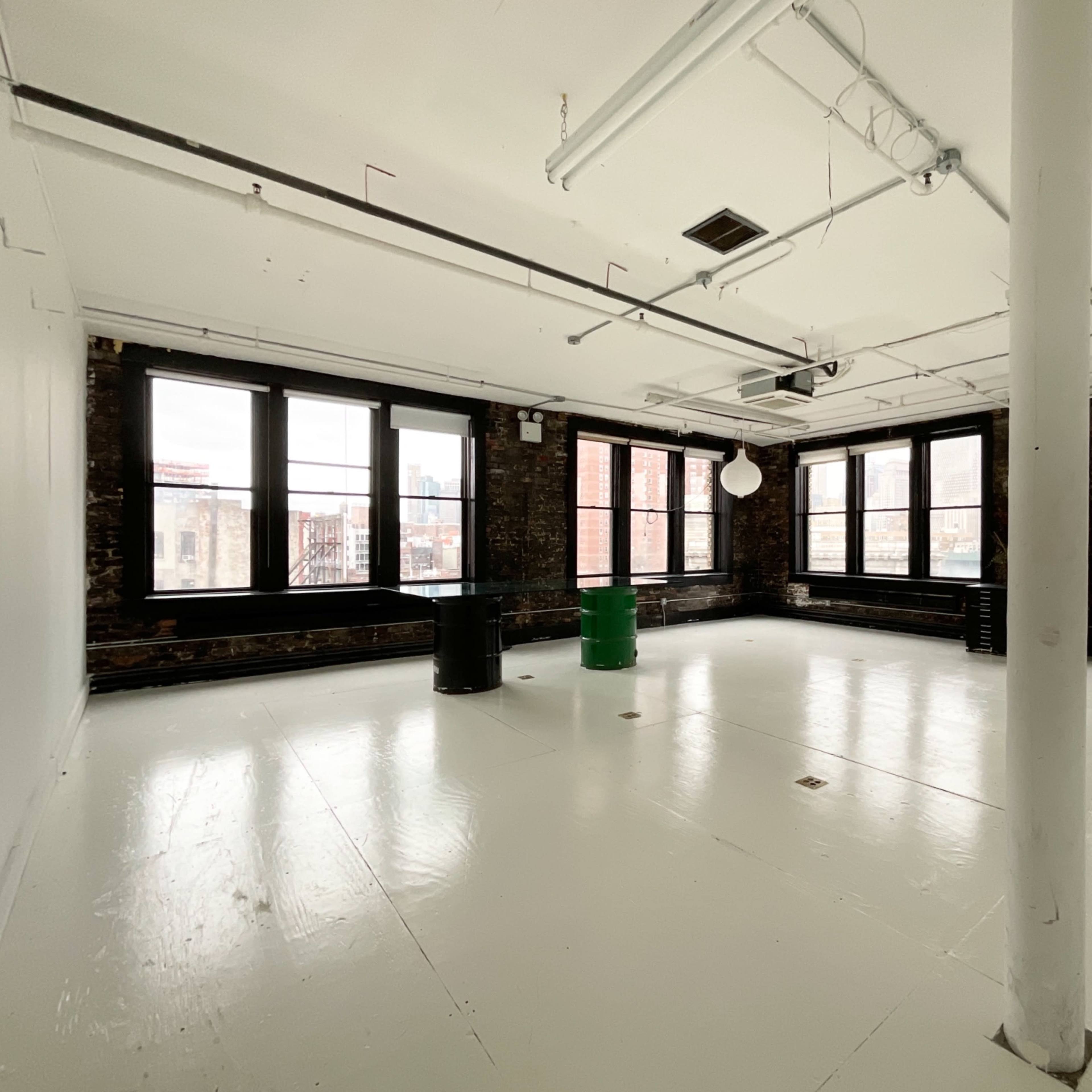A spacious, empty room with white walls, a shiny floor, and large windows overlooking an urban landscape.