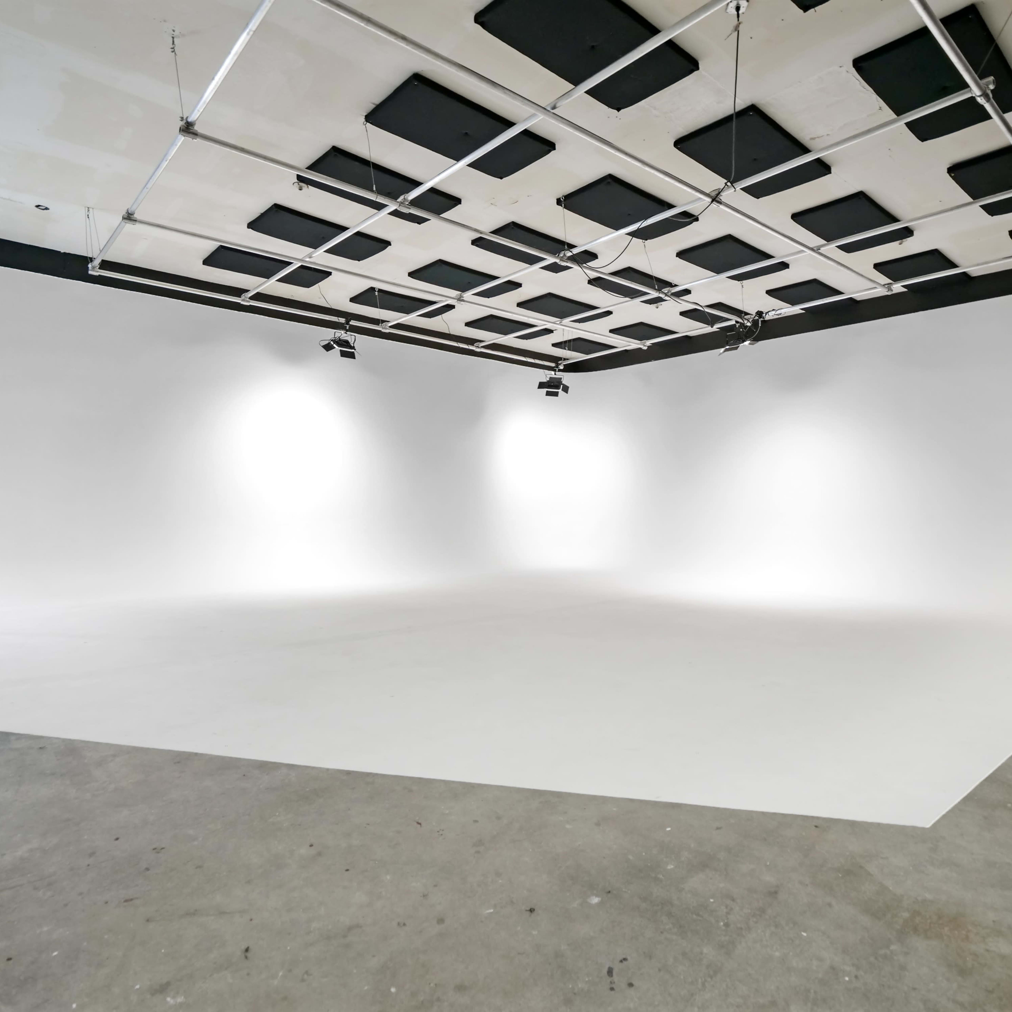 A spacious photo studio with white walls and a seamless backdrop, equipped with overhead lighting.