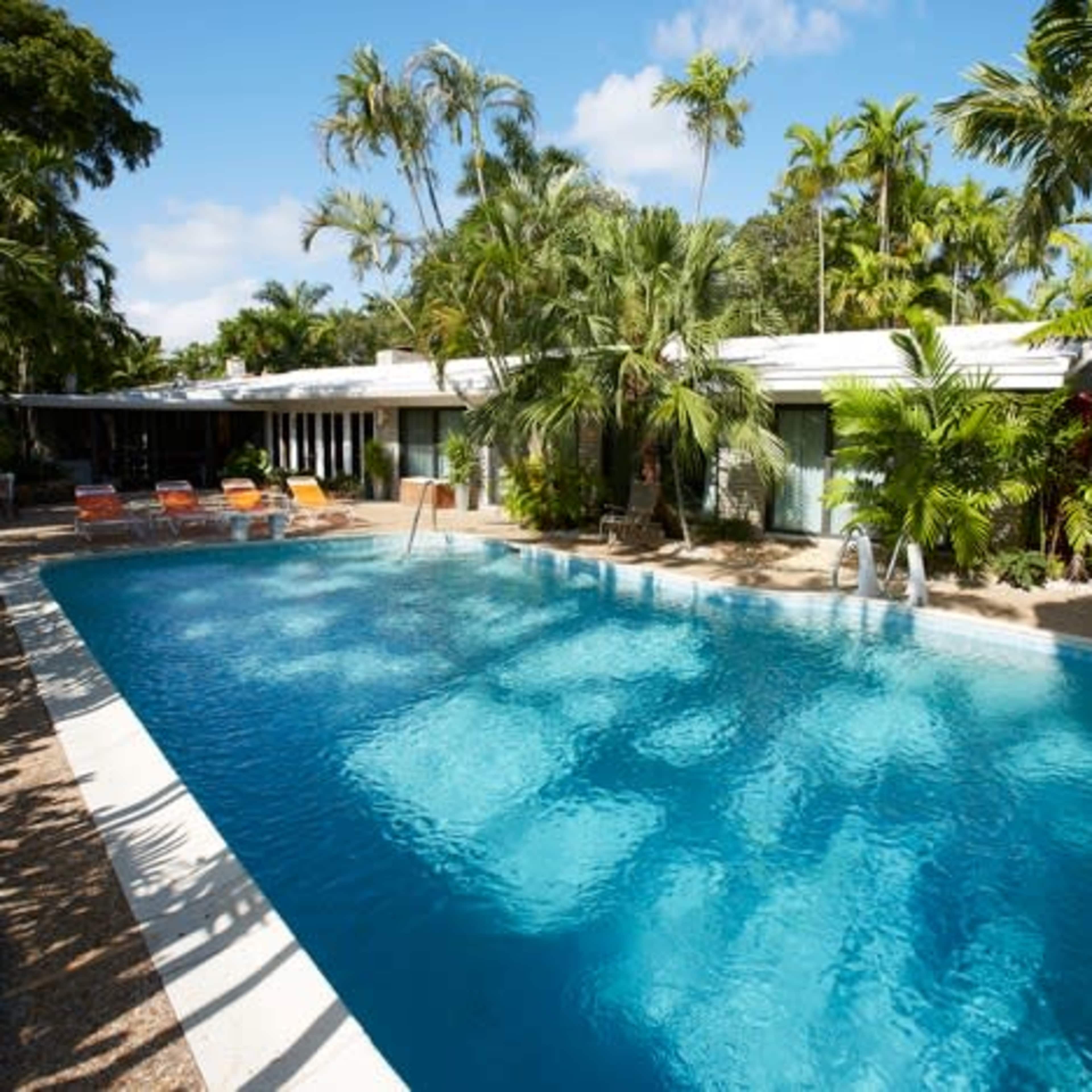A large swimming pool surrounded by tropical plants and a modern building in the background.