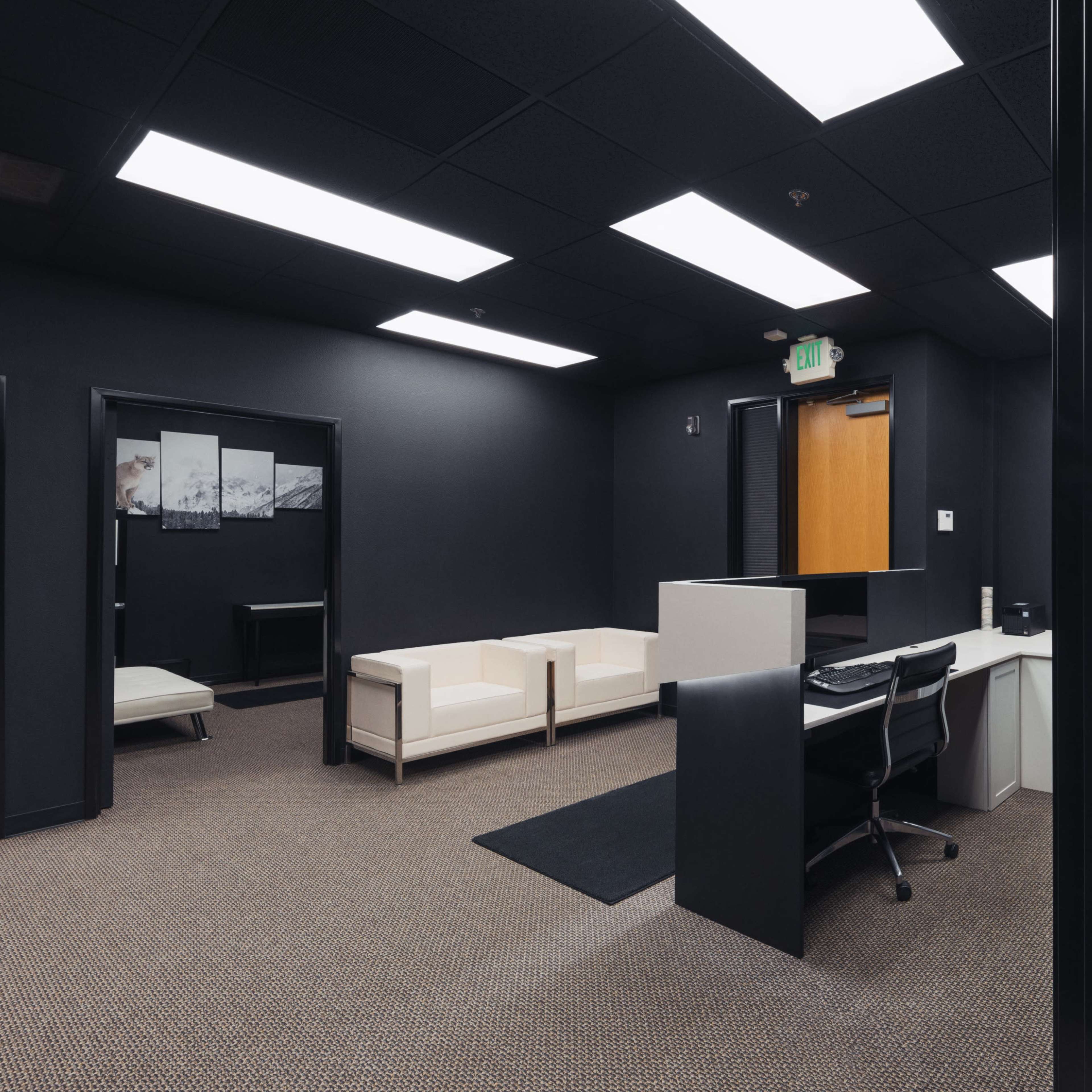 A modern office space featuring a reception area with a white desk, seating area with a white couch, and dark walls.