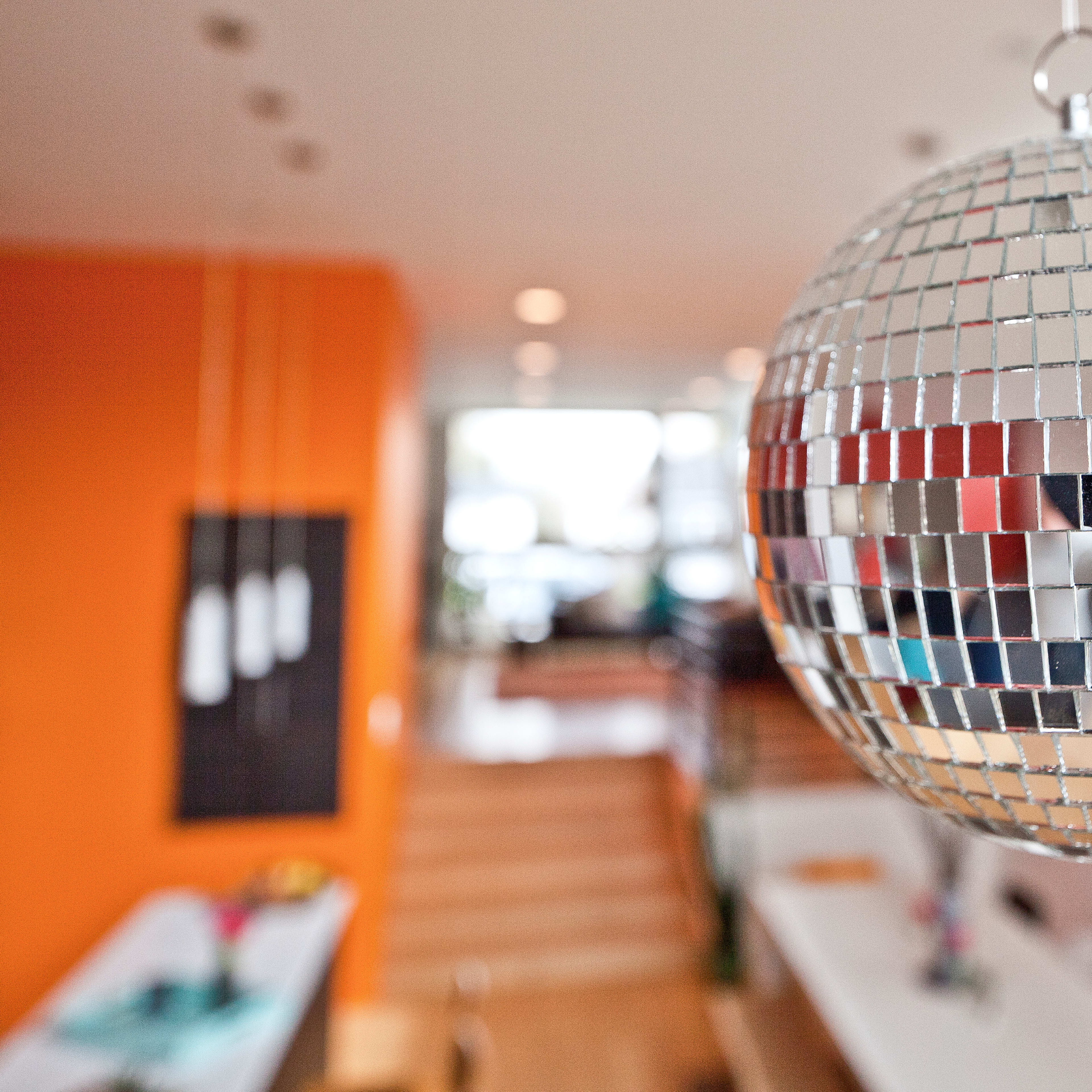 A reflective disco ball hangs from the ceiling in a brightly colored room with a wooden staircase in the background.