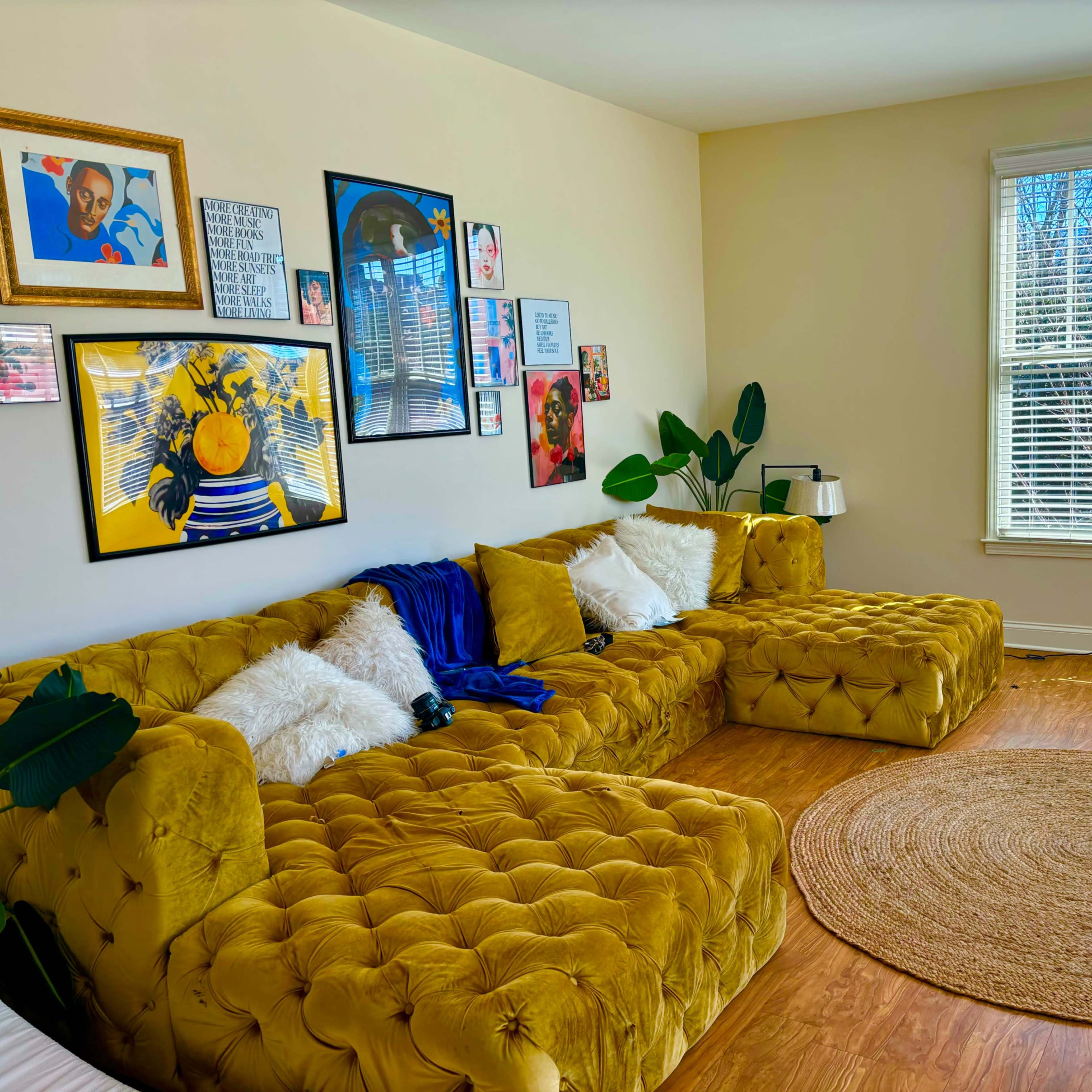 The scene features a bright living room with a yellow tufted sectional sofa, round jute rug, and large windows allowing natural light.