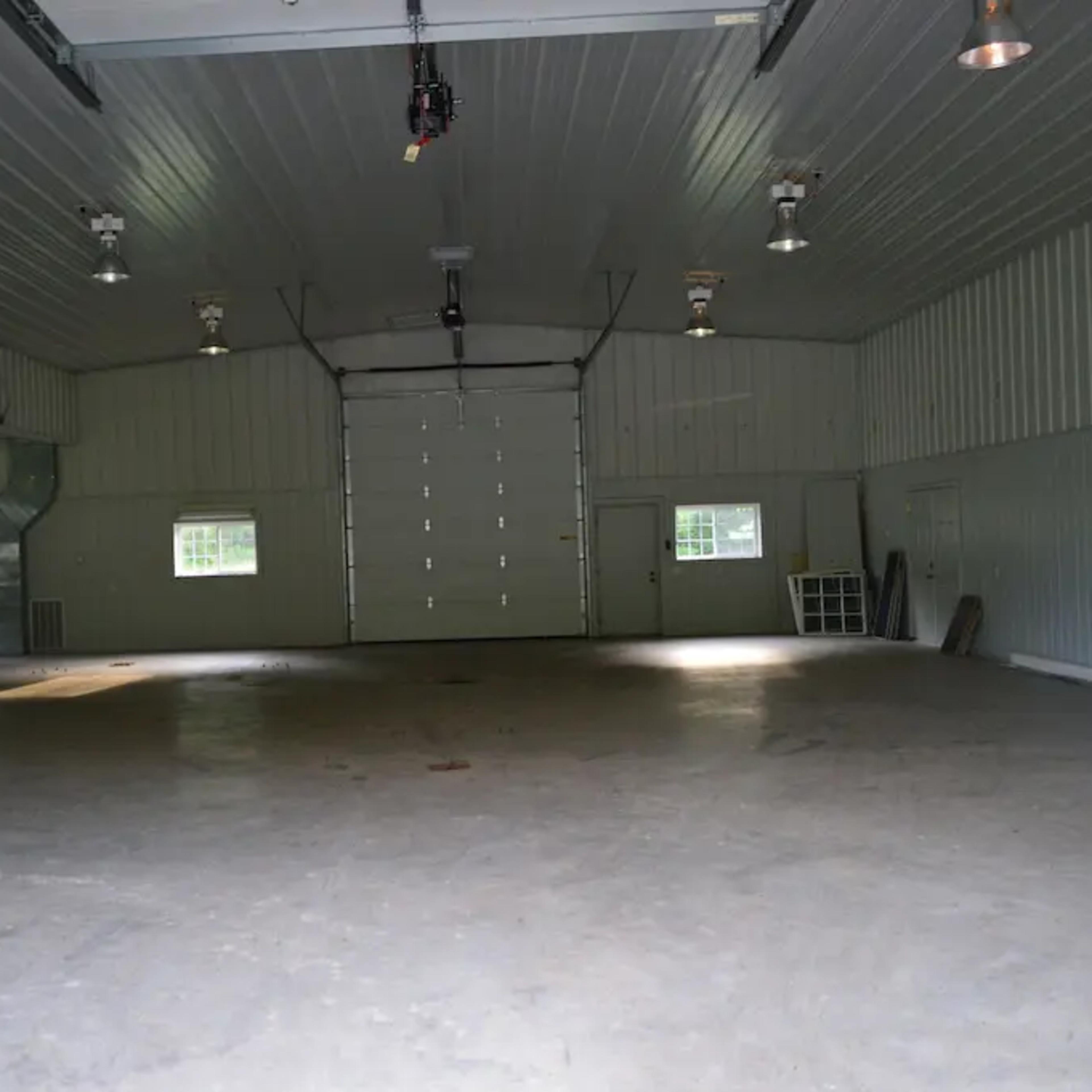 An empty metal-walled garage with a large overhead door and several lights illuminating the space.