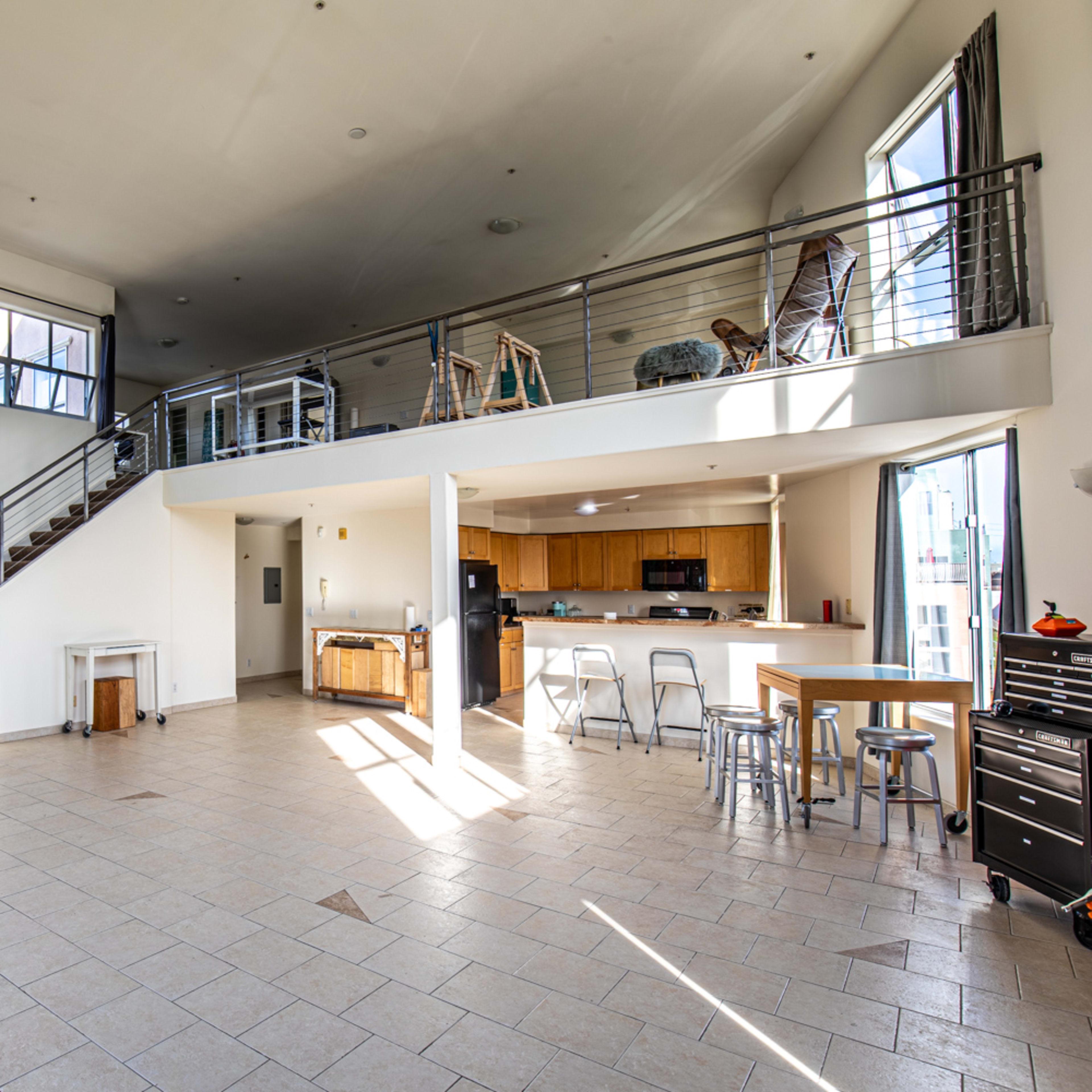A spacious, modern interior with a staircase leading to a loft area, featuring large windows and a kitchen area with seating.