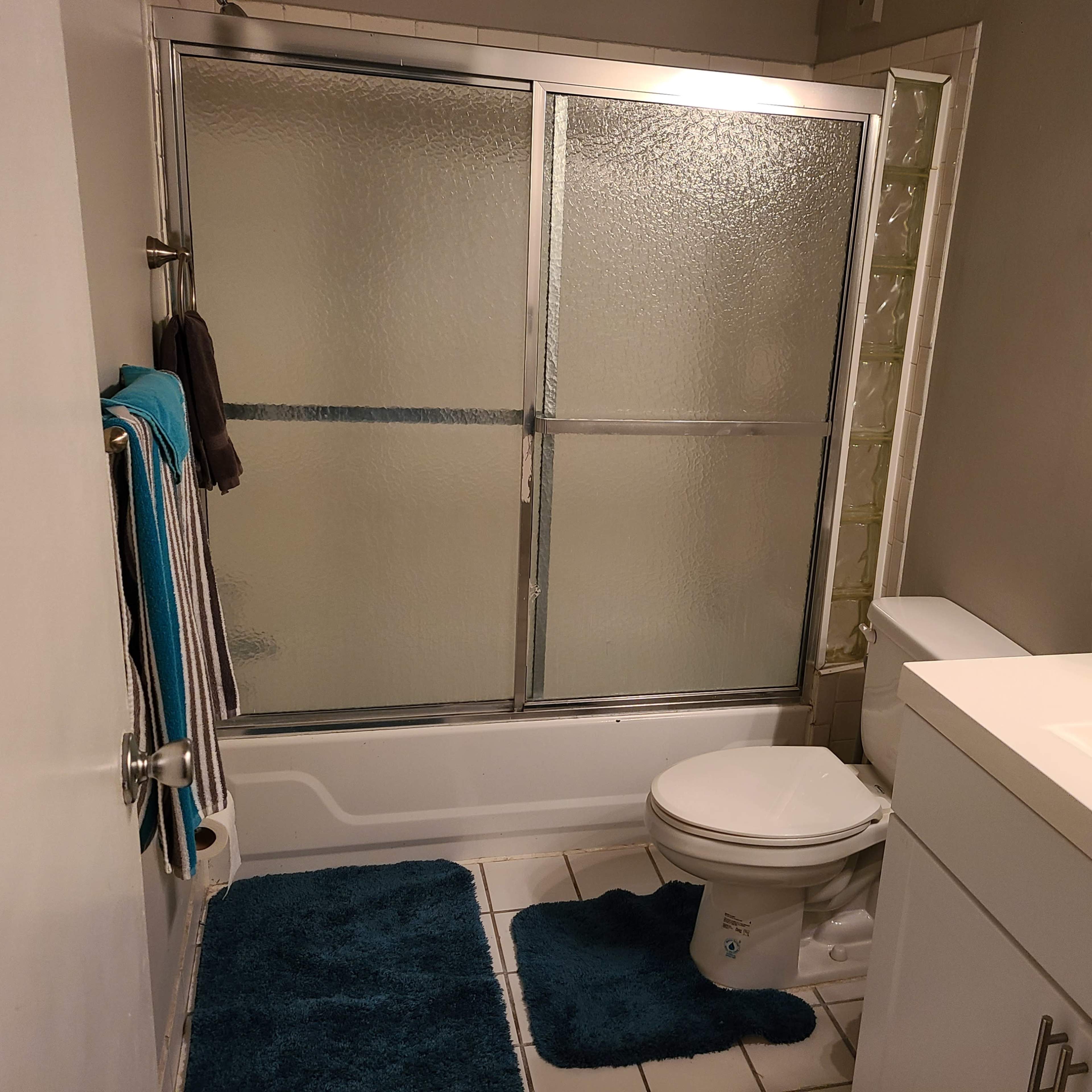 A bathroom featuring a glass shower enclosure, a toilet, a sink with a countertop, and towels hanging on a rack.