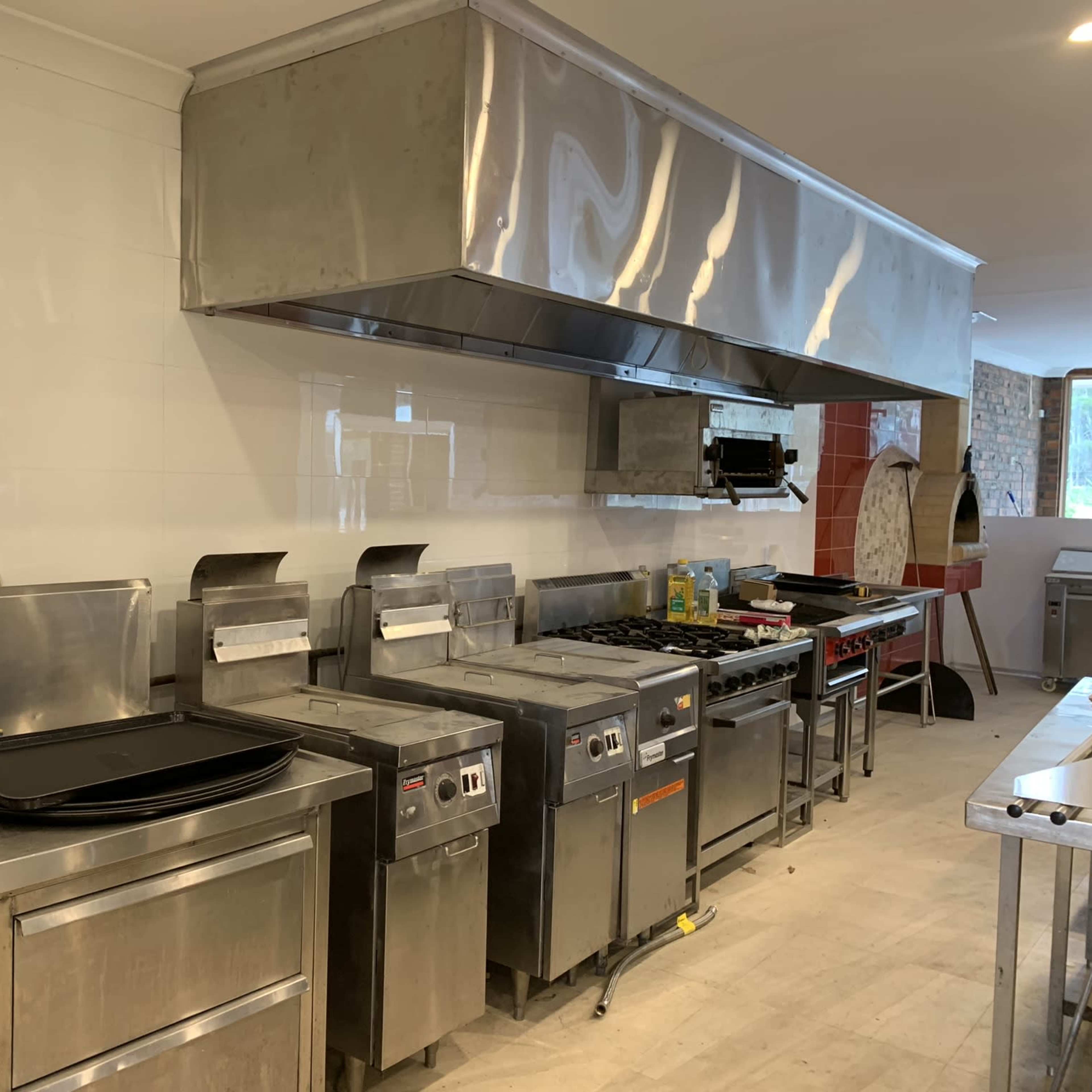 A commercial kitchen equipped with stainless steel appliances, including ovens, fryers, and a large exhaust hood.