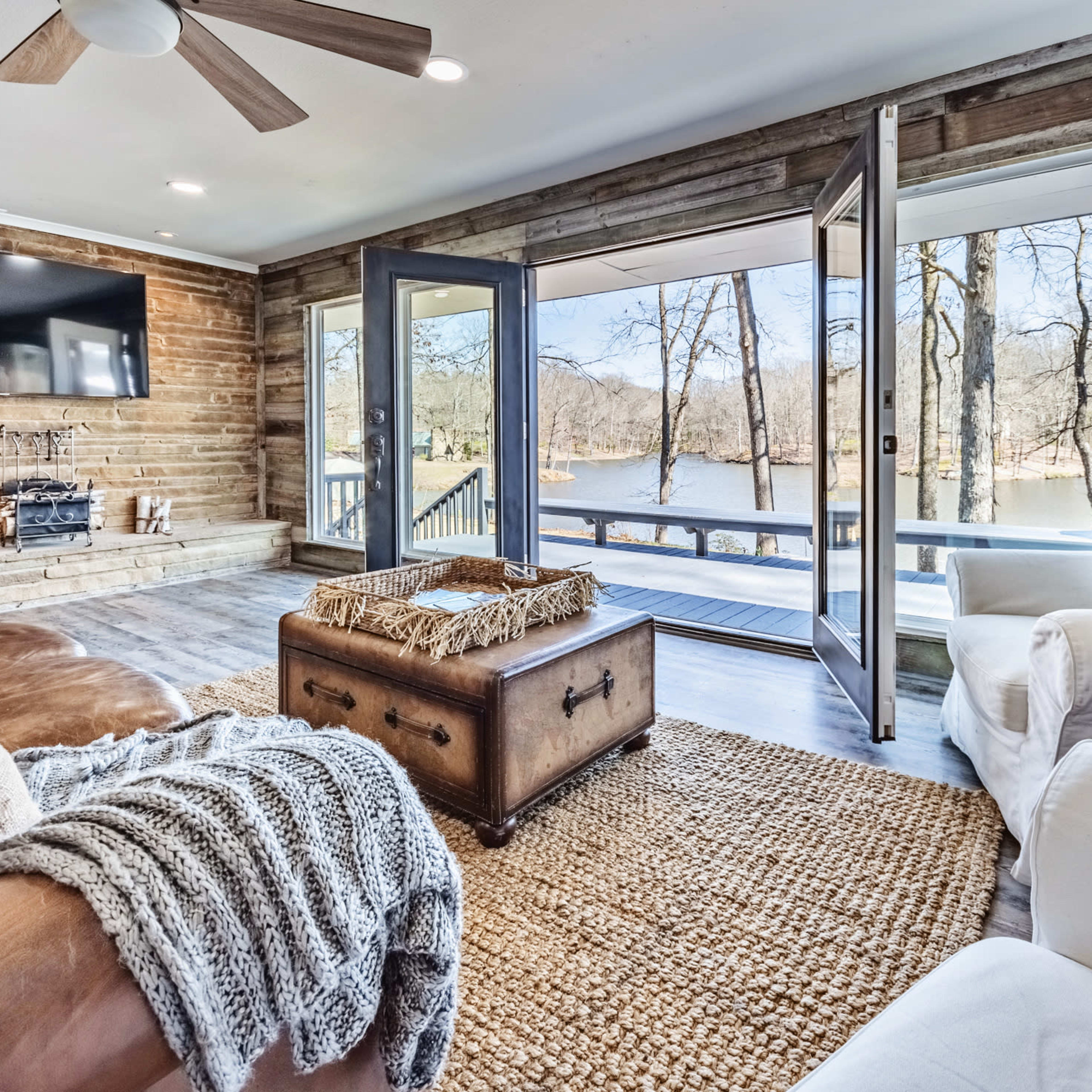 A cozy living room with large windows overlooking a lake, featuring wooden walls, comfortable seating, and a coffee table.