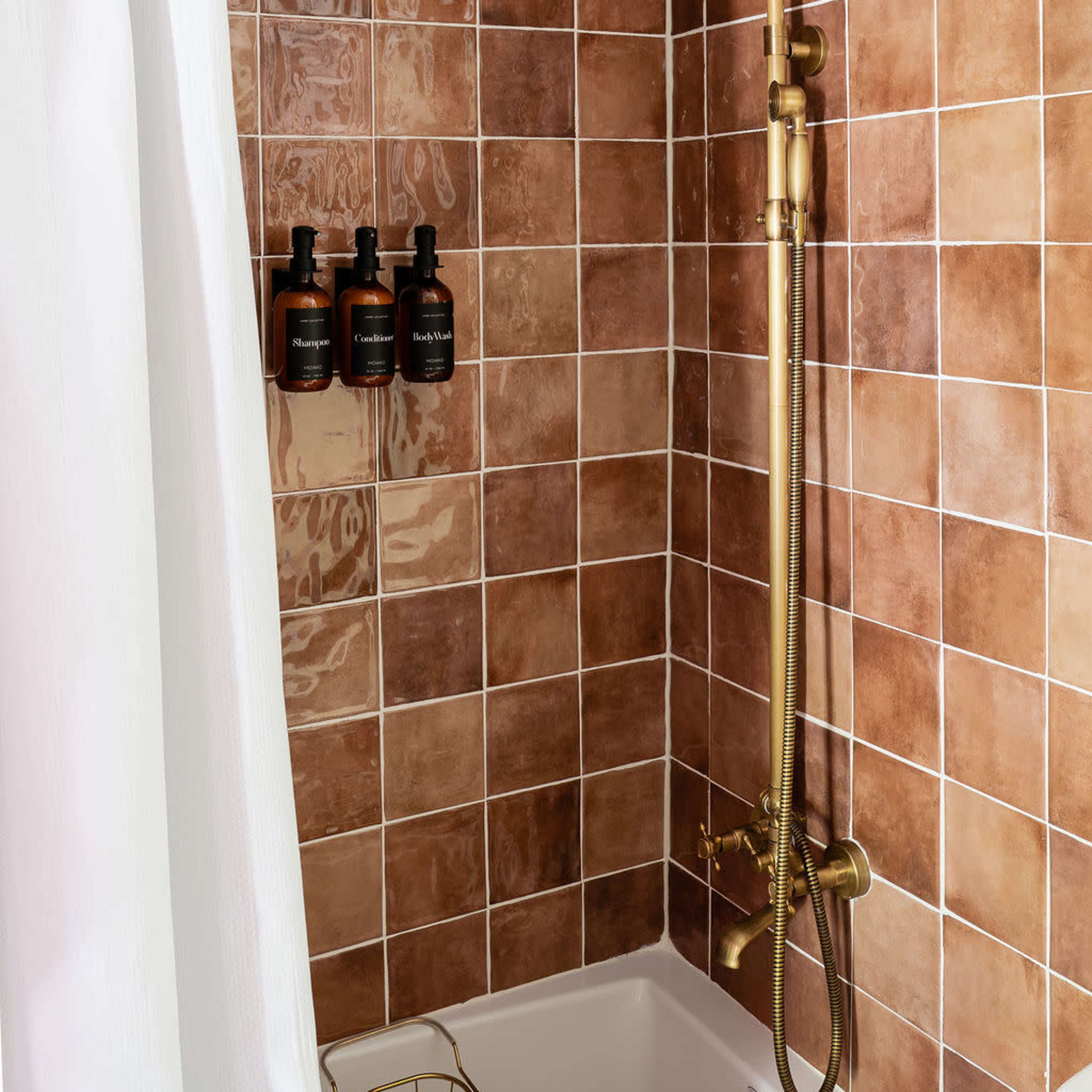 A modern shower enclosed by a white curtain, featuring a gold showerhead and tiled walls in varying shades of brown.