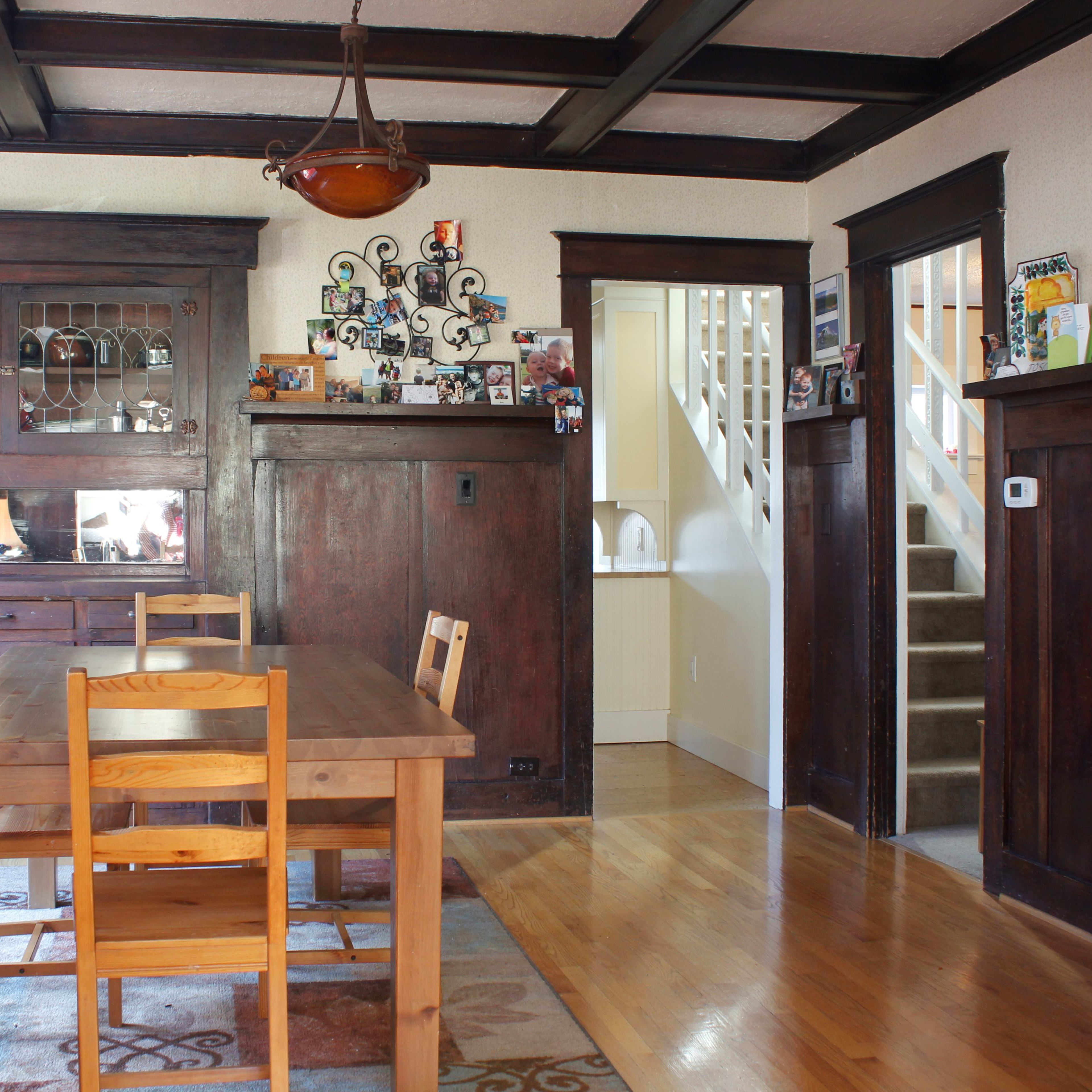 A dining area featuring a wooden table with four chairs, a sideboard against the wall, and a staircase leading to an upper level.