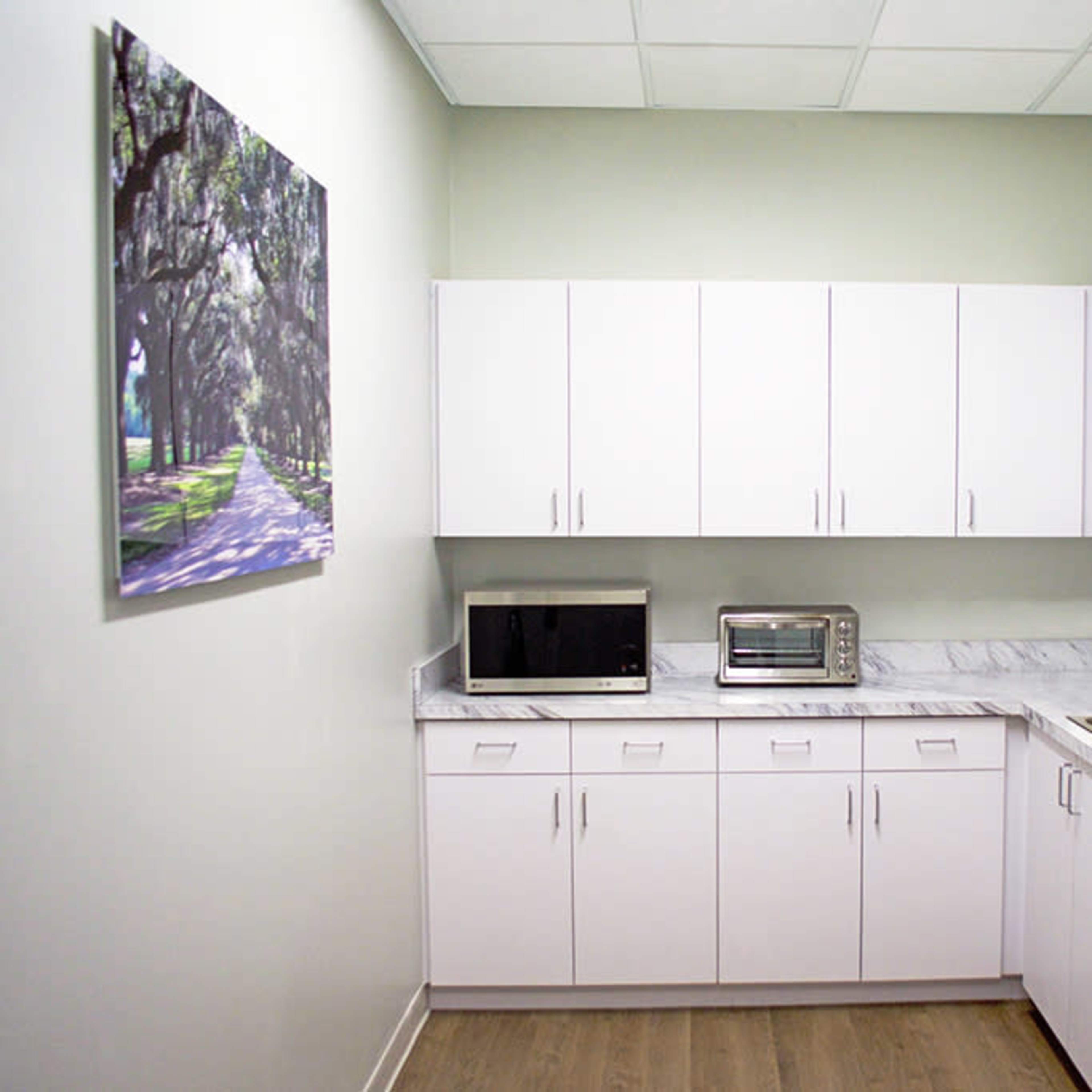 A modern kitchen with white cabinets, a microwave, a toaster oven, and a stainless steel refrigerator, set against a light green wall.