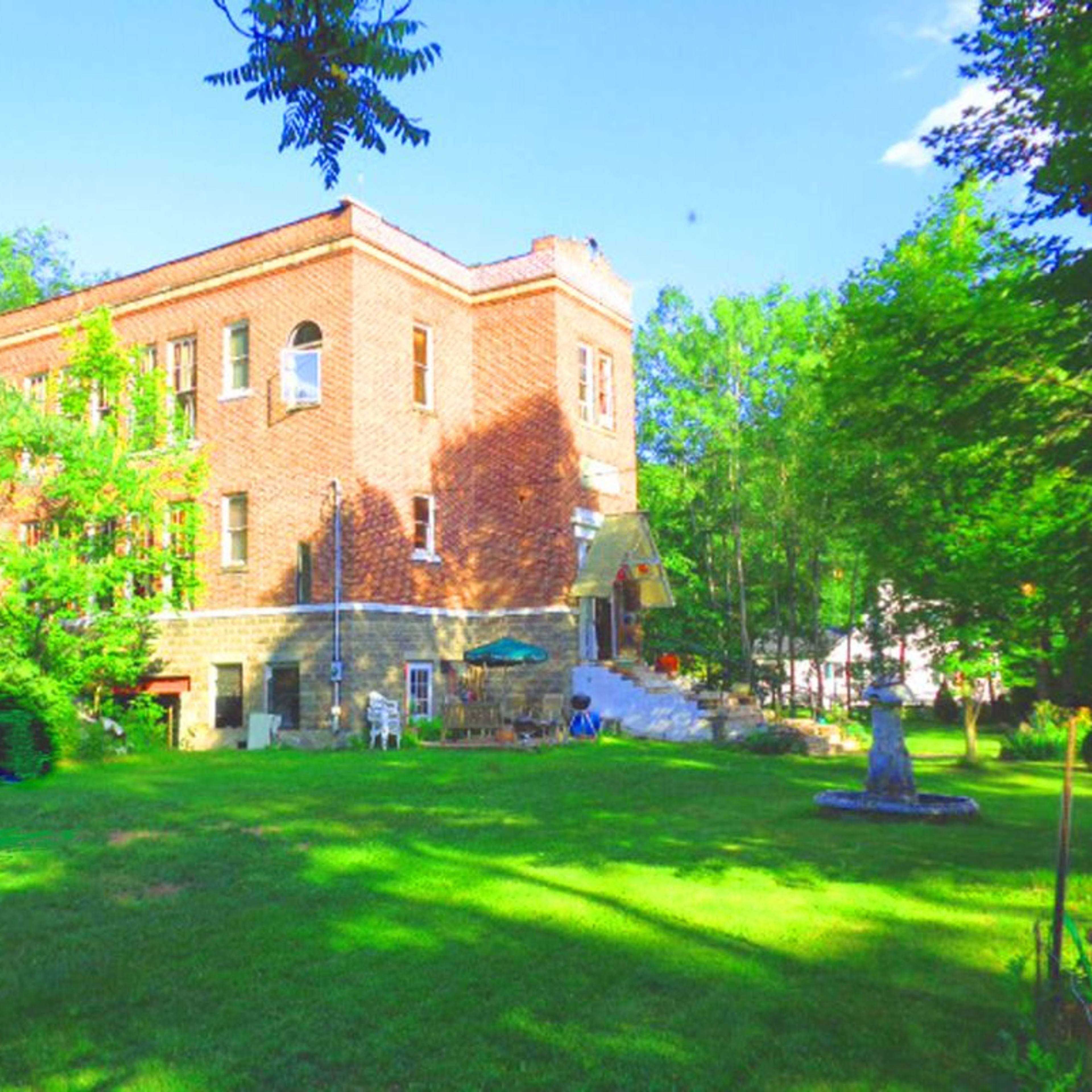 A large brick building surrounded by greenery and a well-maintained lawn.