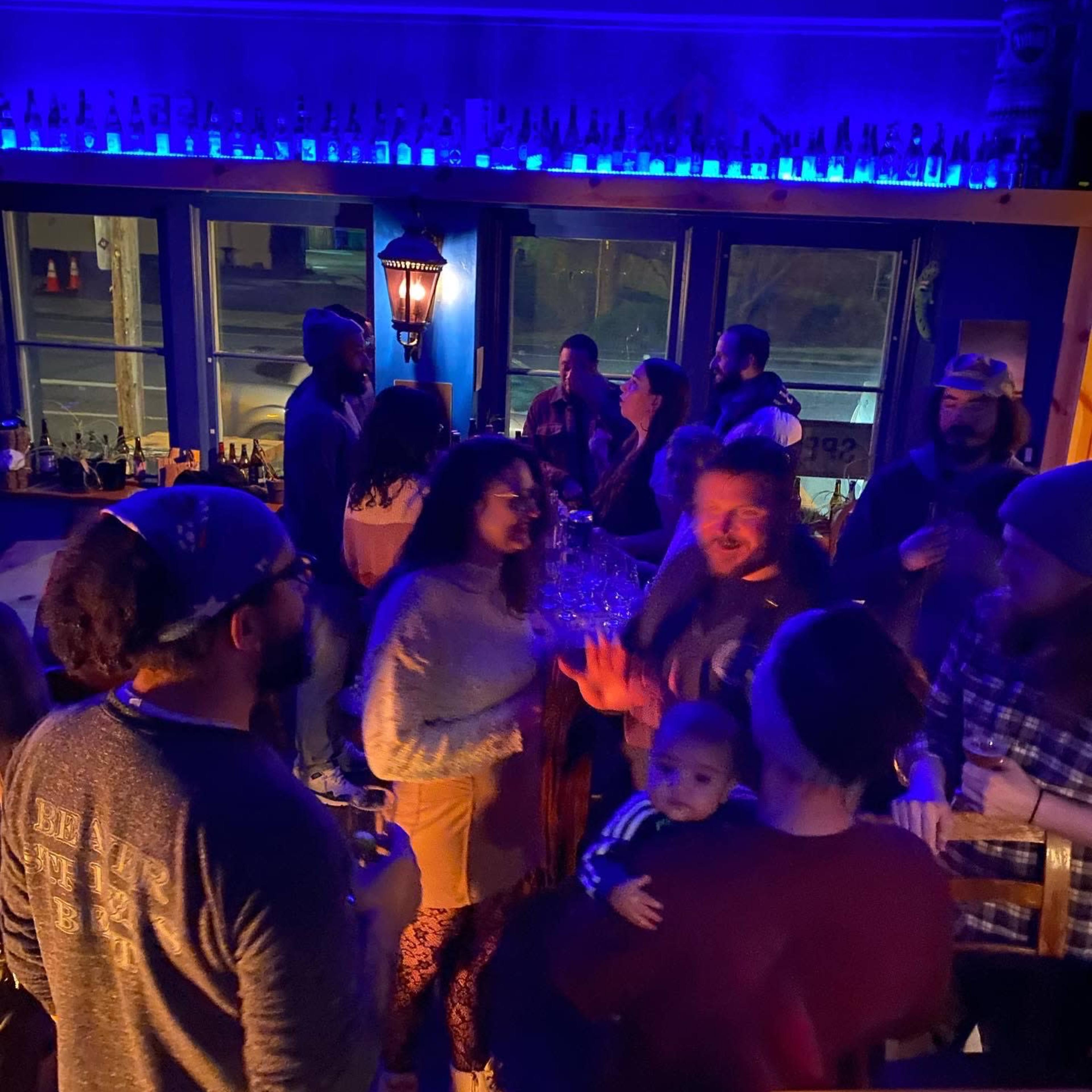 A group of people socializes and drinks in a dimly lit bar with blue lighting.