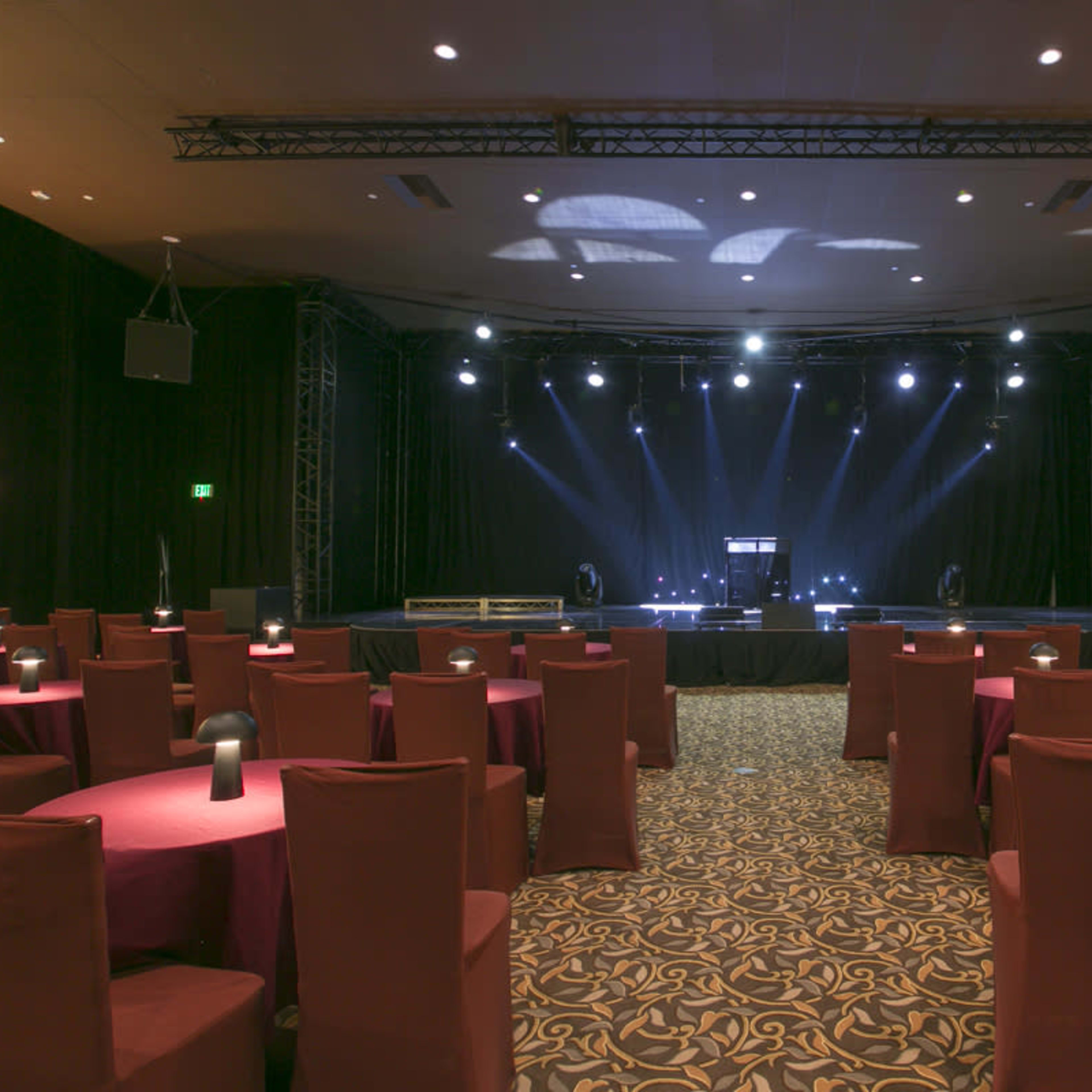 A performance stage with lighting set up in a room filled with round tables and chairs.