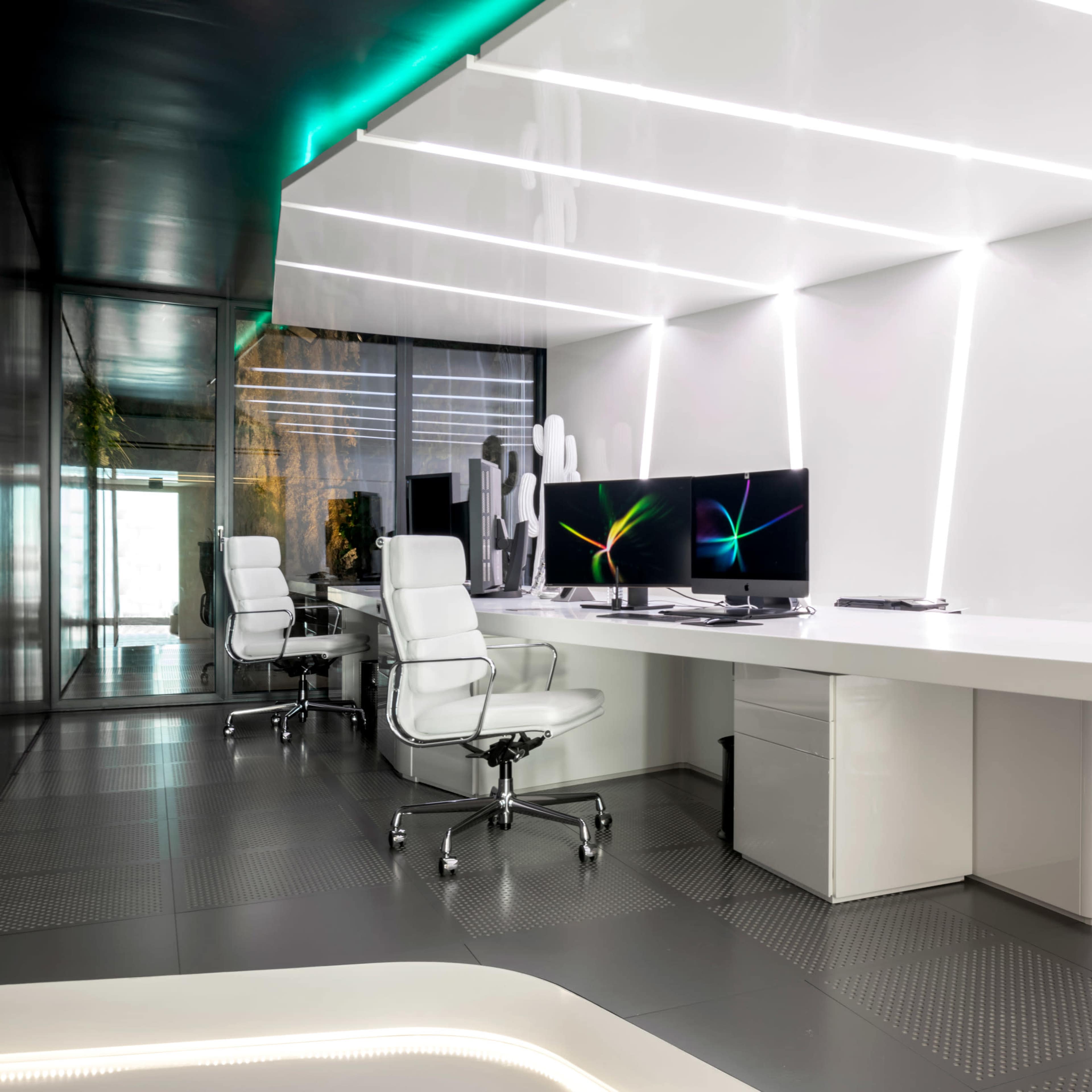 A modern office space with a white desk, ergonomic chairs, and a large monitor set against a sleek, brightly lit design.