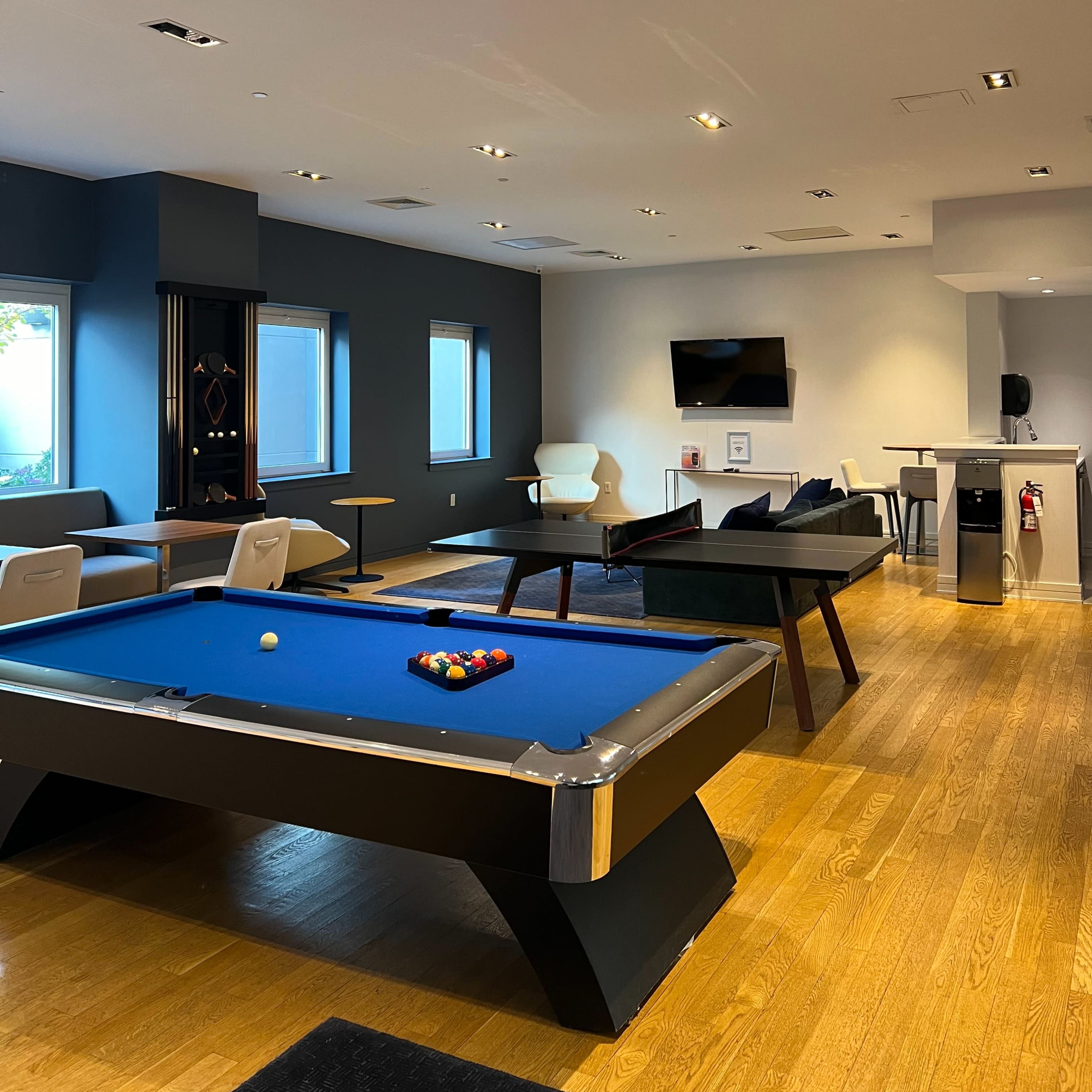 A modern game room featuring a blue pool table, a seating area, and a television on the wall.