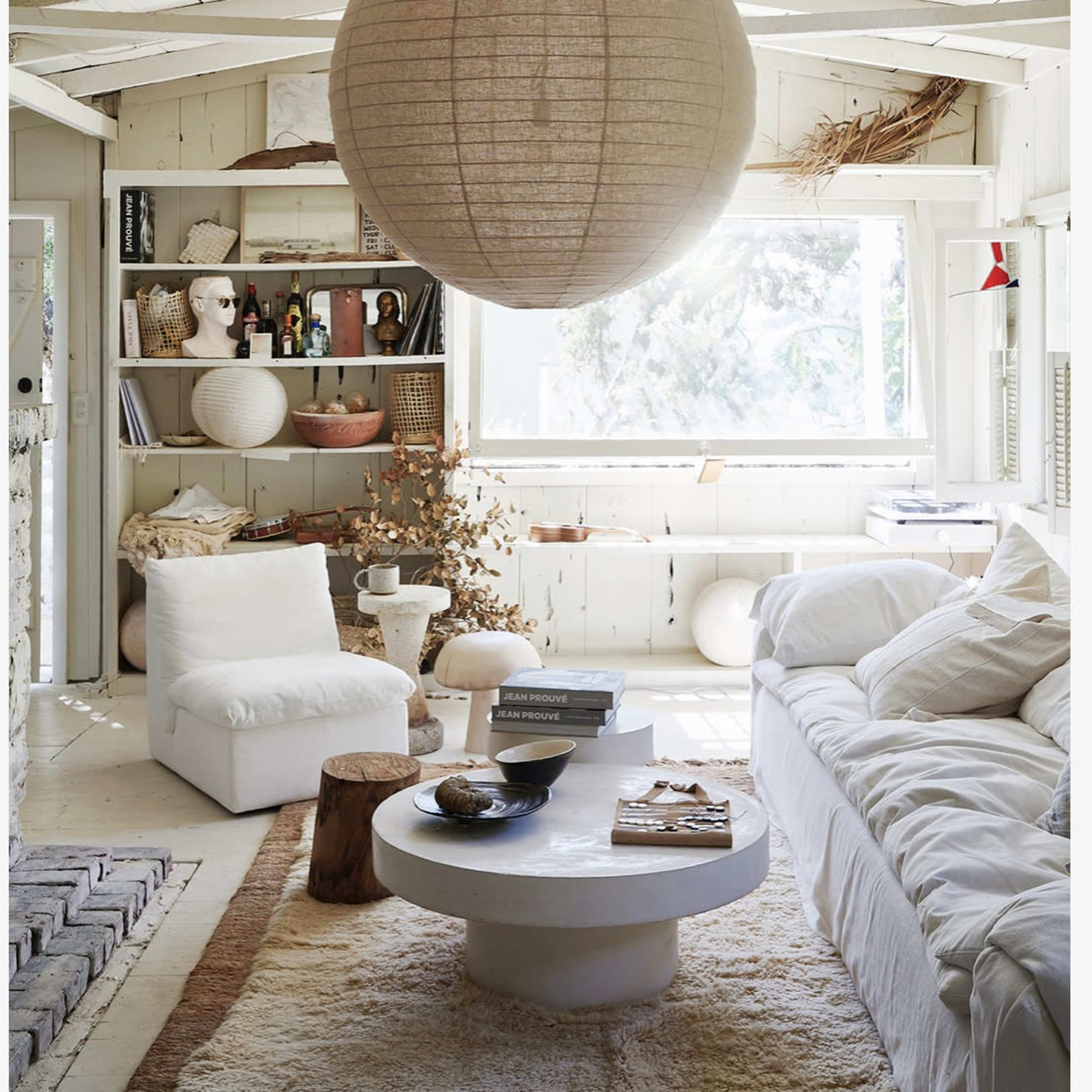 A spacious living room features a large paper lantern hanging overhead, with a white couch, circular coffee table, and shelves displaying various decor items.