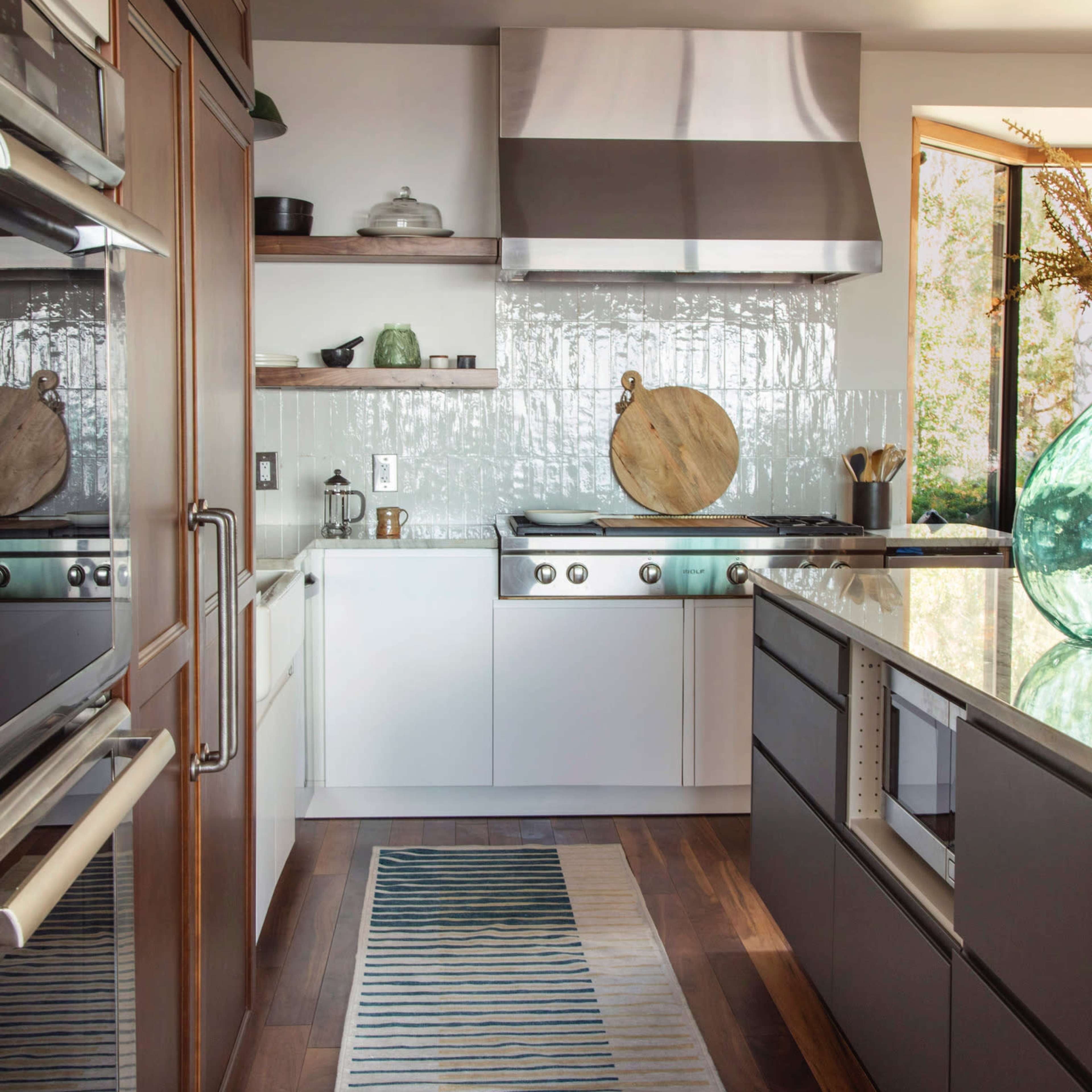 A modern kitchen features stainless steel appliances, a tiled backsplash, and a striped runner rug over hardwood flooring.