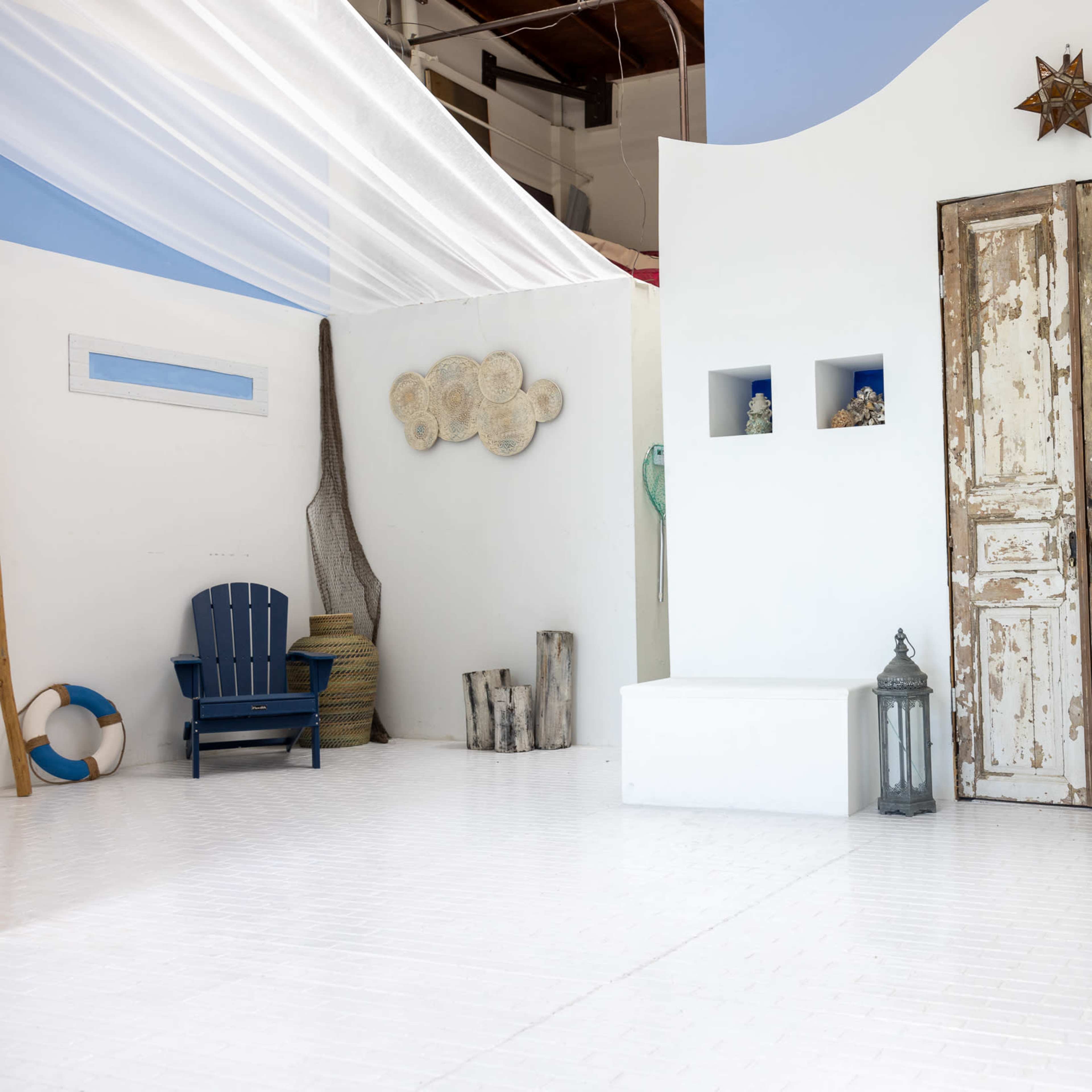 A minimalist indoor space features white walls, a pair of weathered double doors, and decorative elements such as lanterns and a wooden chair.