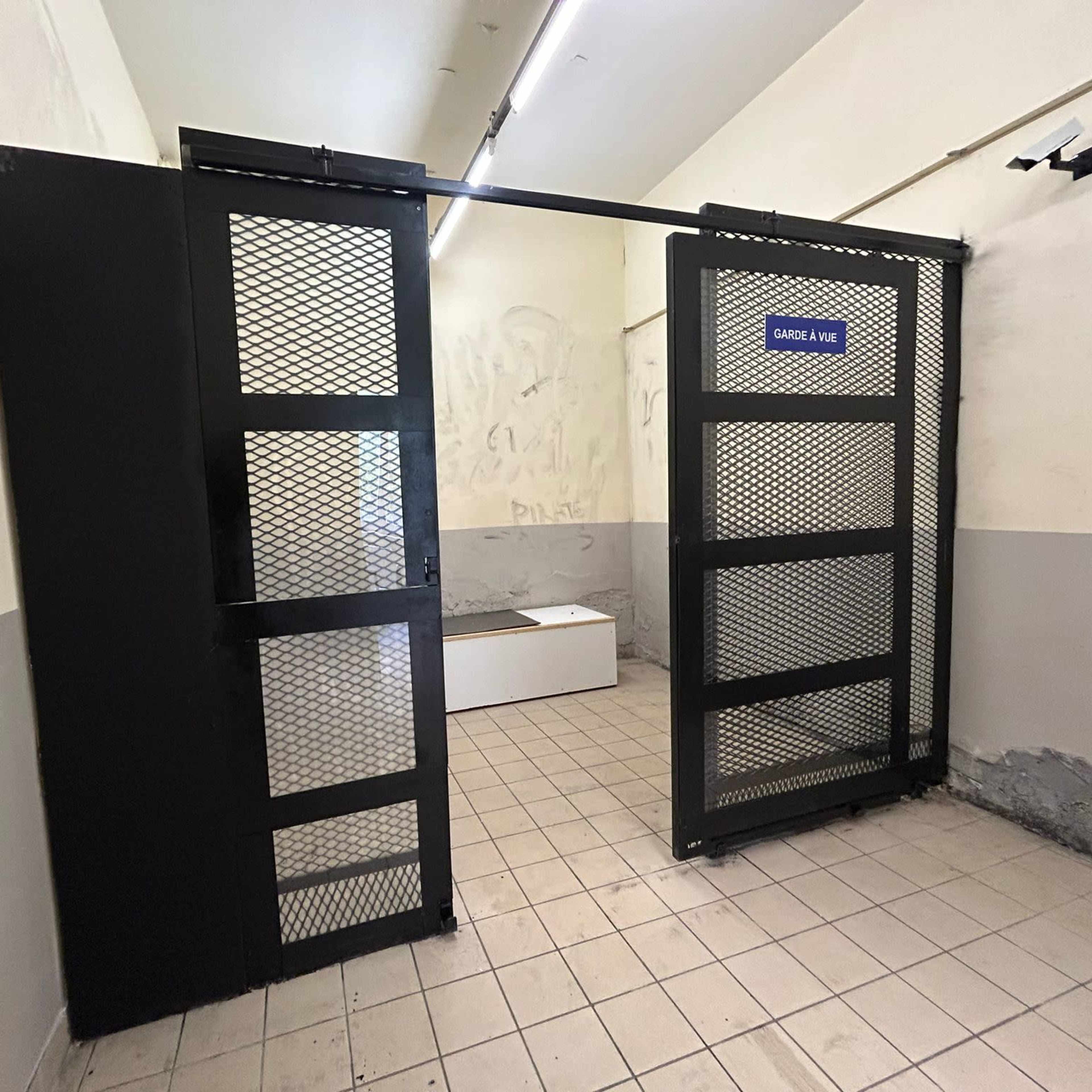 A large metal gate, labeled "GARDEN LV," partially open in a vacant room with tiled flooring and bare walls.