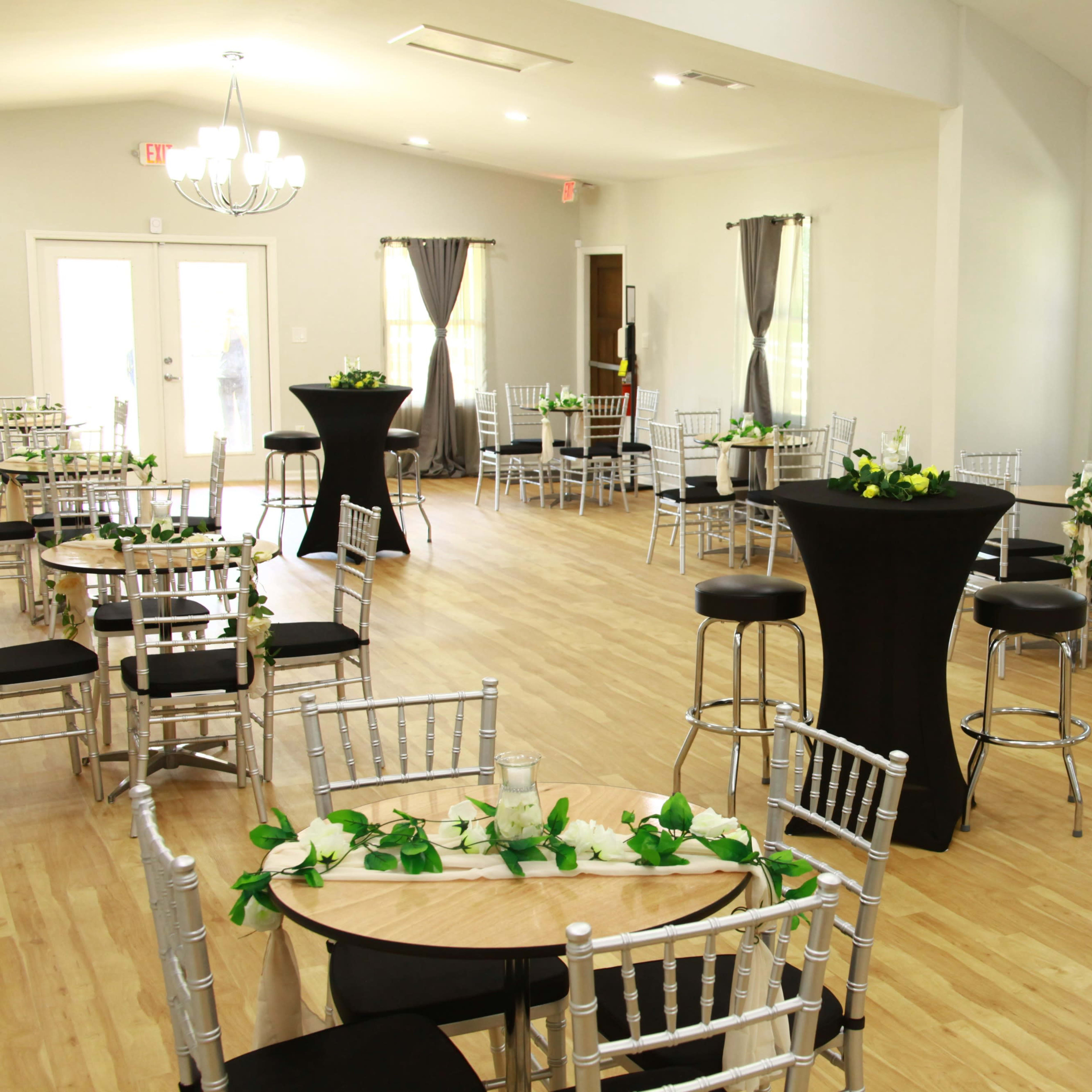 A spacious event room with silver chiavari chairs, black cocktail tables, and floral decorations on the tables.