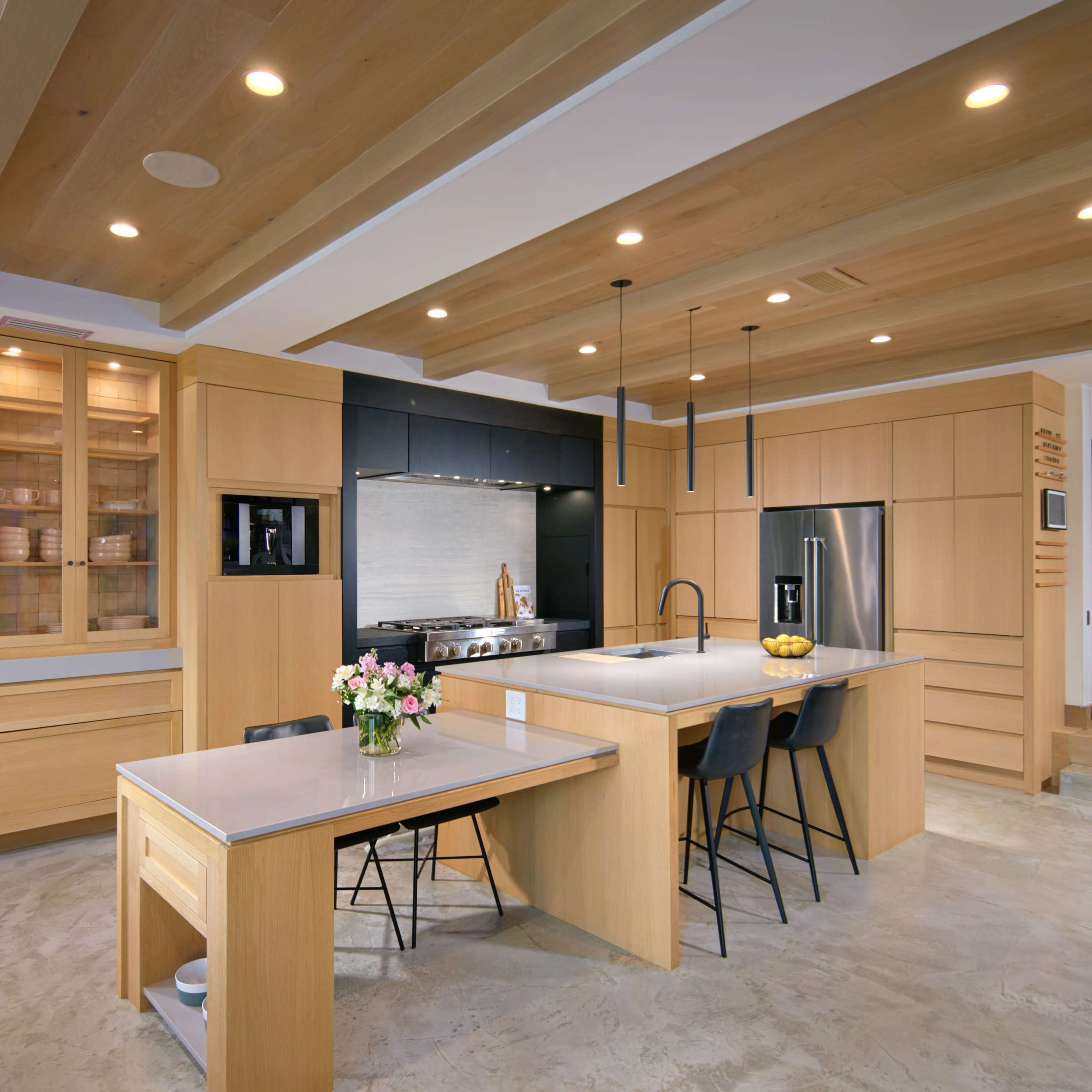 A modern kitchen with wooden cabinetry, a central island, and sleek appliances, featuring a mix of light wood and gray surfaces.