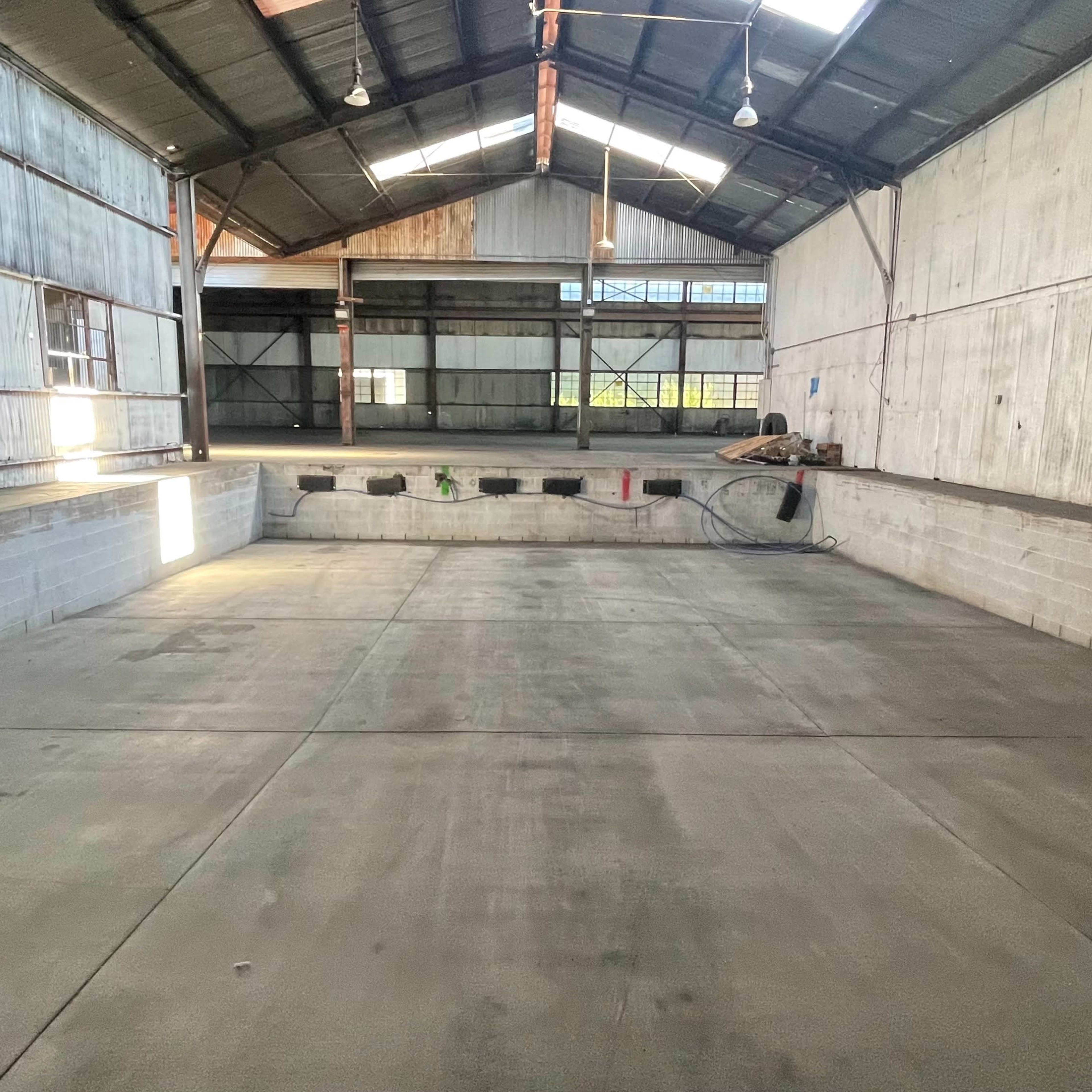 An empty industrial warehouse with a concrete floor, steel beams, and large open spaces.