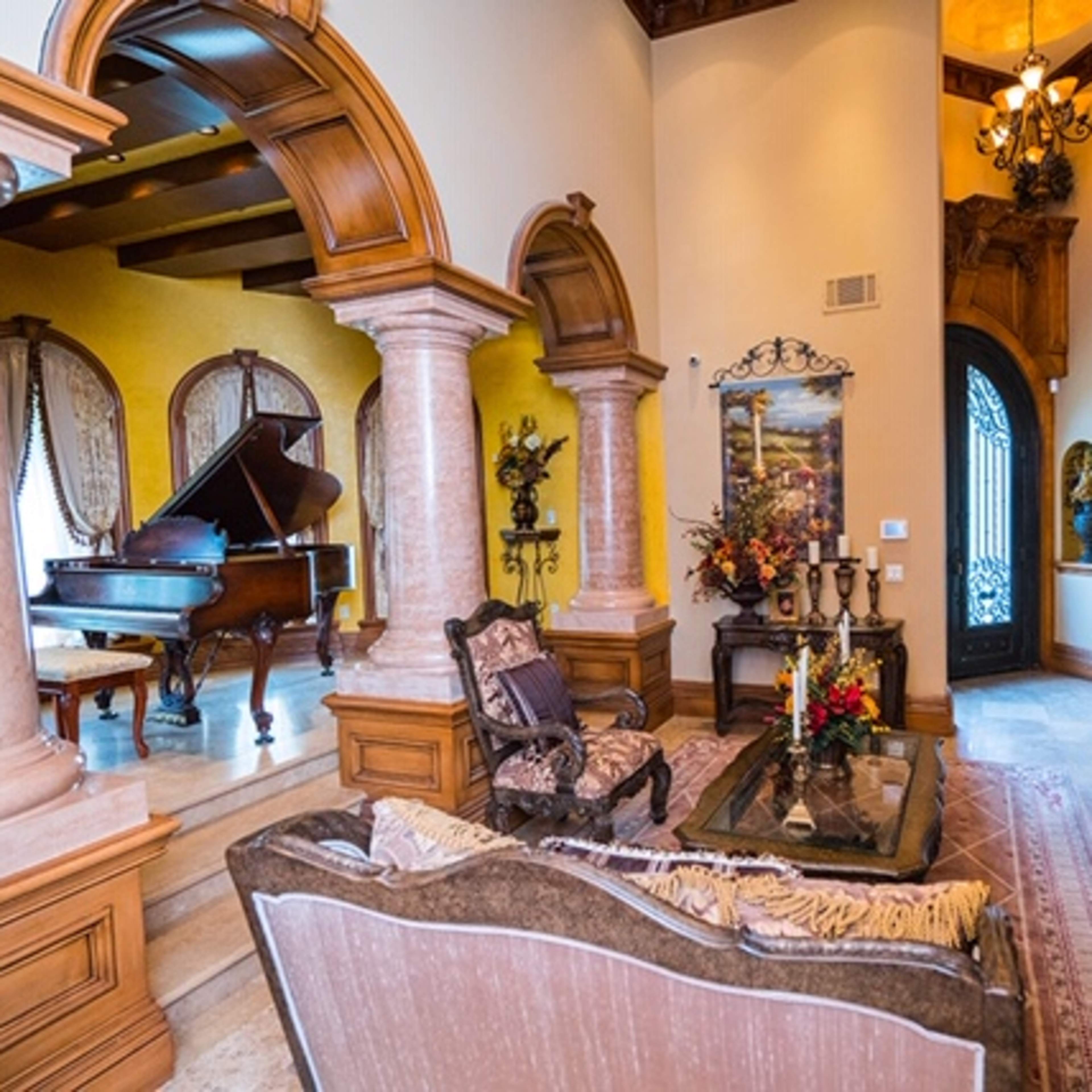 An elegant living room featuring a grand piano, ornate columns, and a well-decorated seating area.