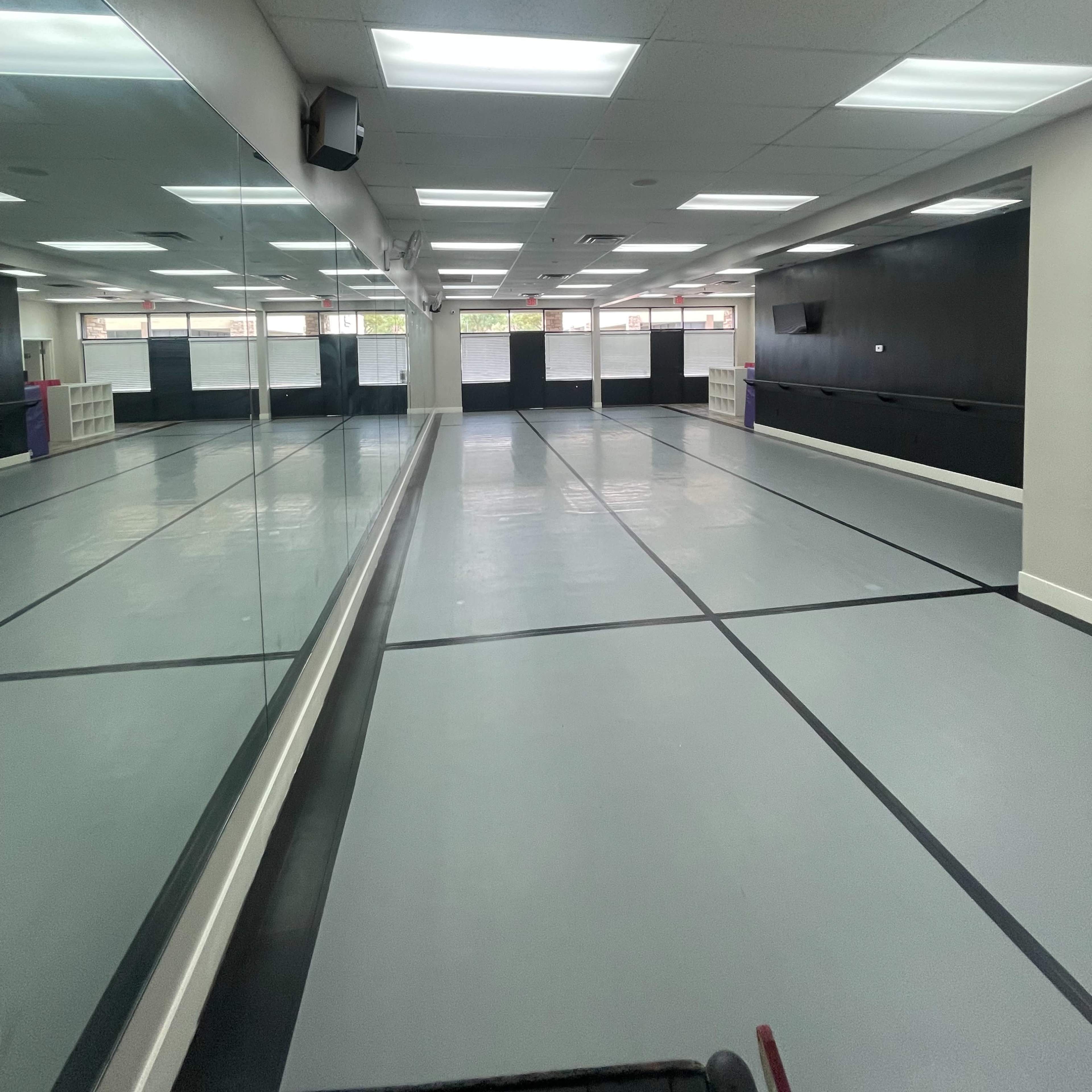 An empty dance studio with mirrored walls and fluorescent lighting.