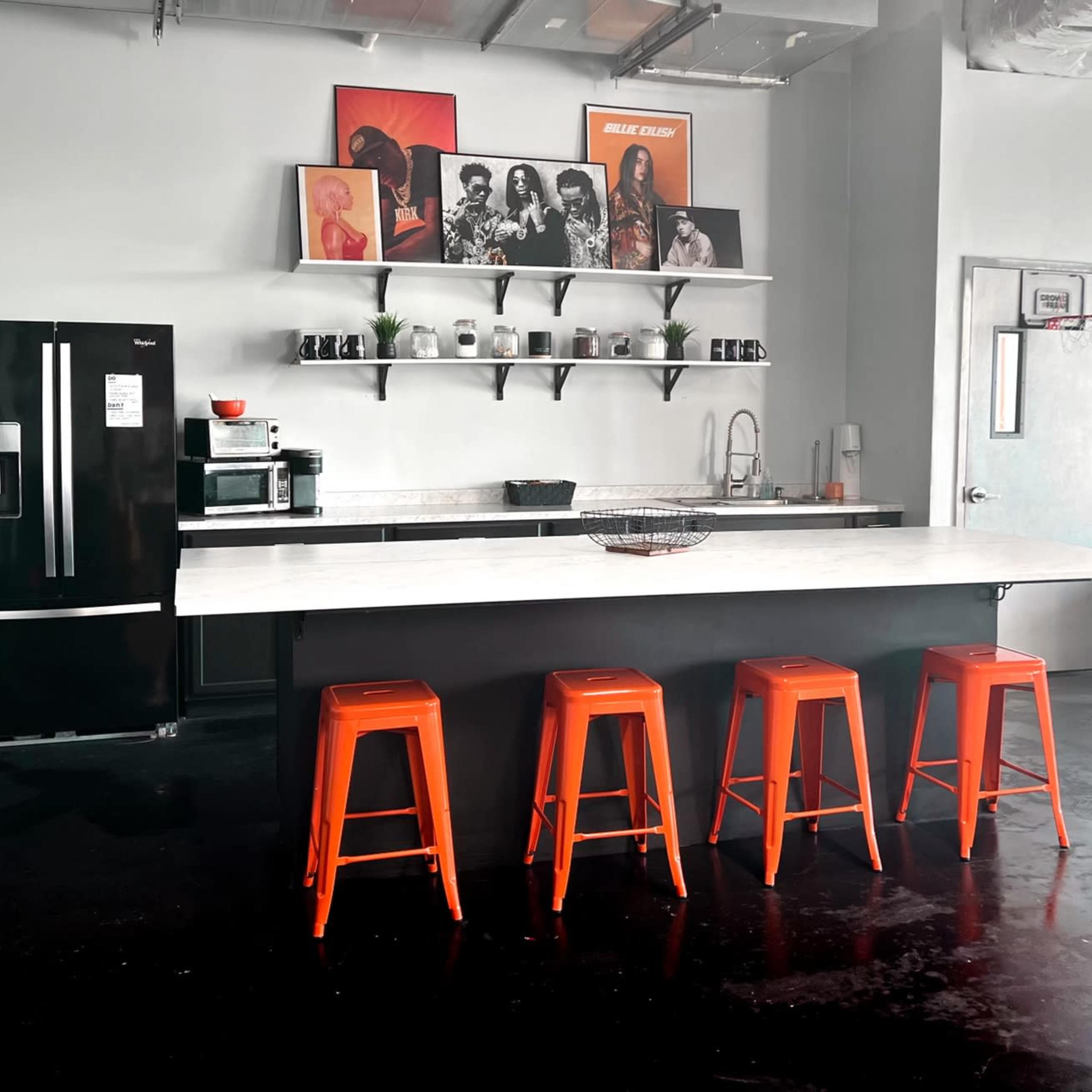 A modern kitchen with a marble island, four orange stools, a black refrigerator, and decorative artwork on the walls.