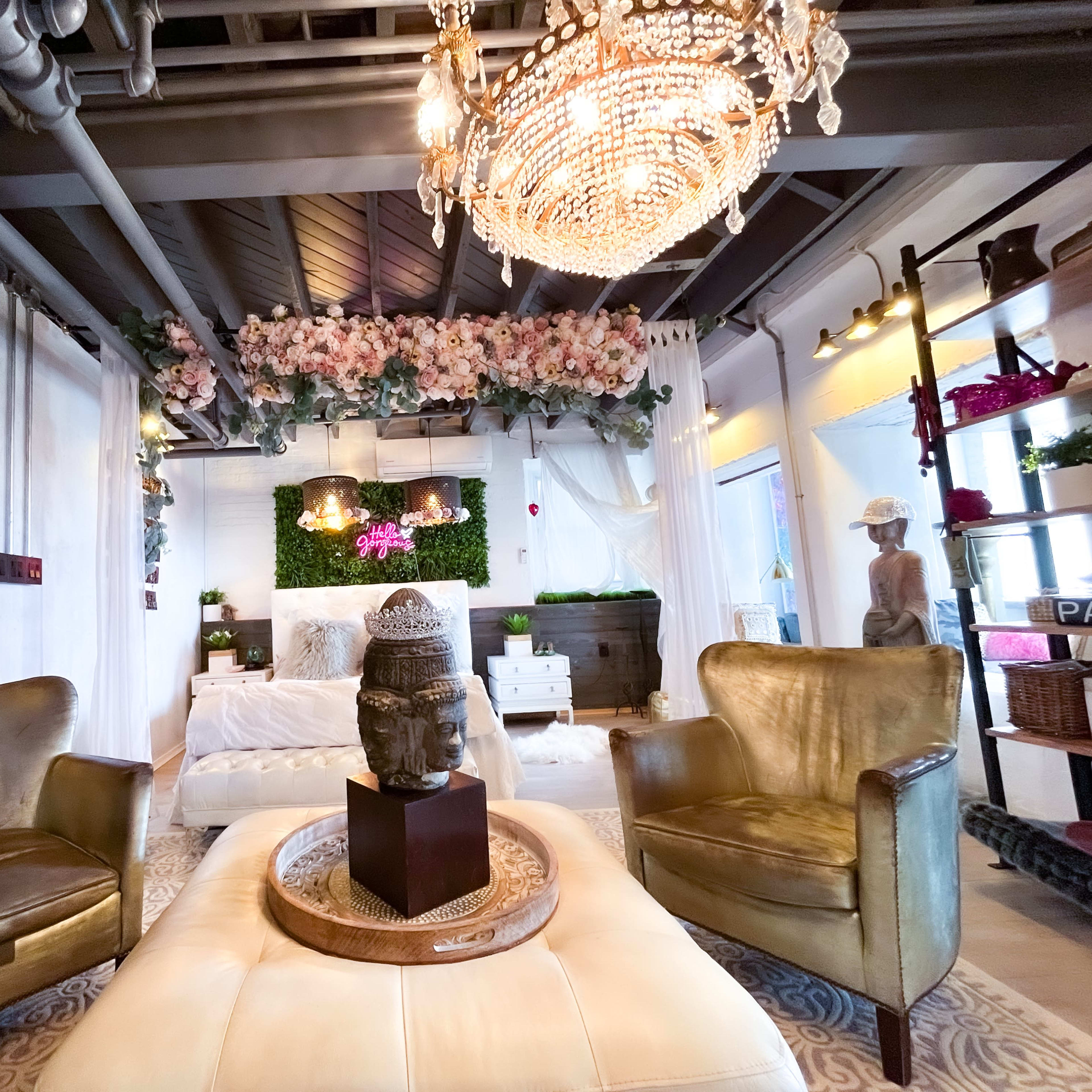 A stylish interior space featuring two gold armchairs, a large ottoman with a decorative statue, and floral decor above a bed.
