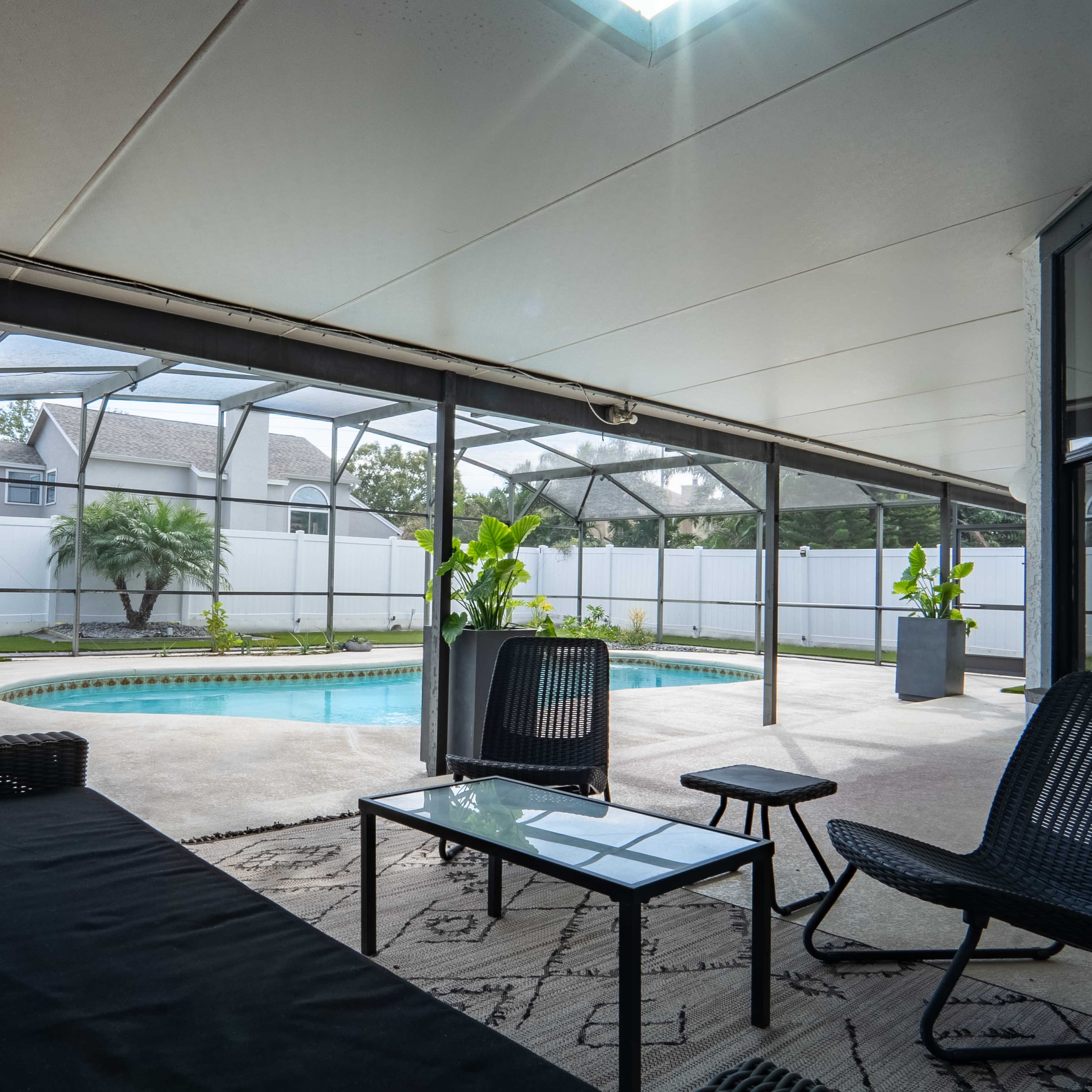 A covered patio area with a view of a swimming pool surrounded by greenery and plants.