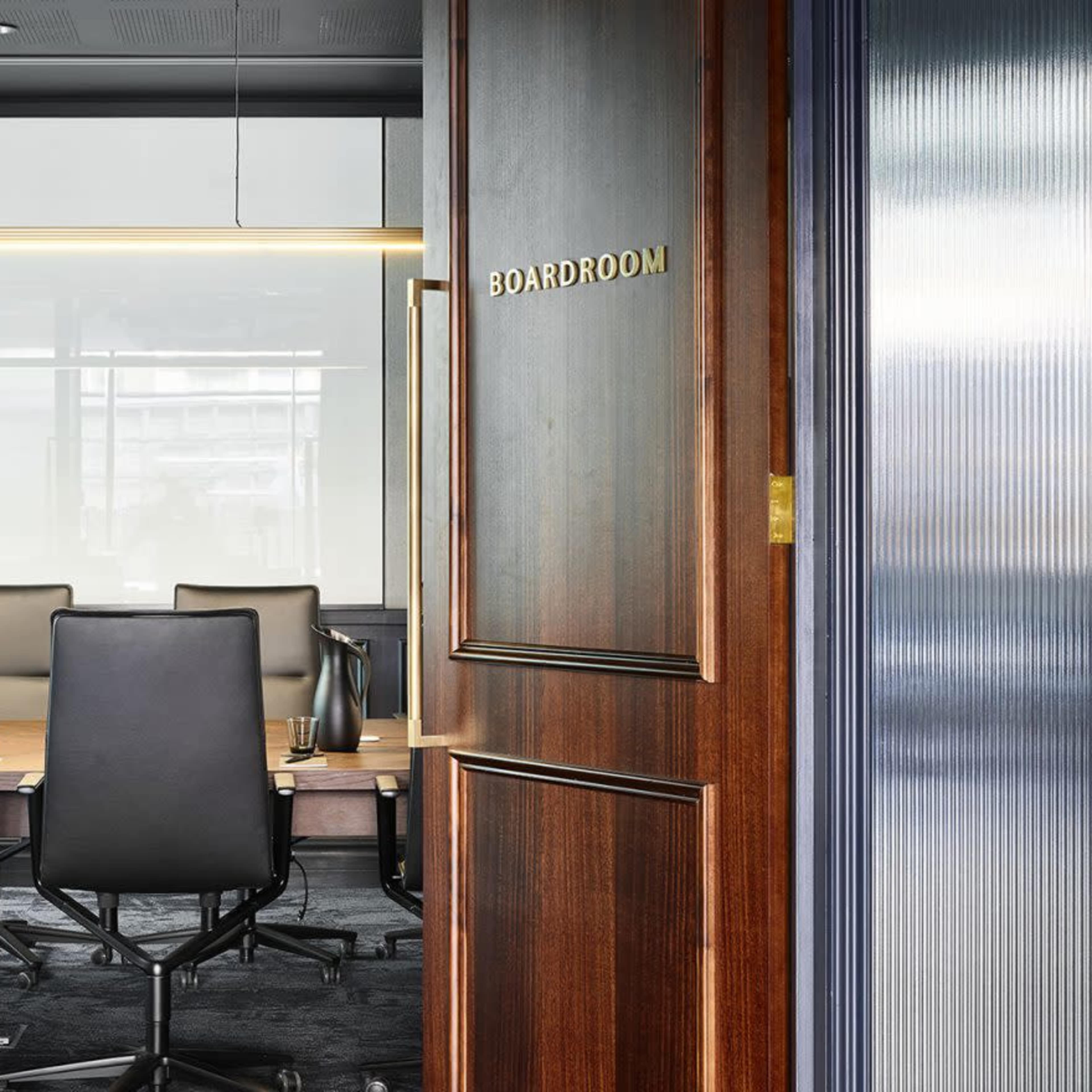A modern boardroom with a long table and ergonomic chairs, viewed through open wooden double doors.
