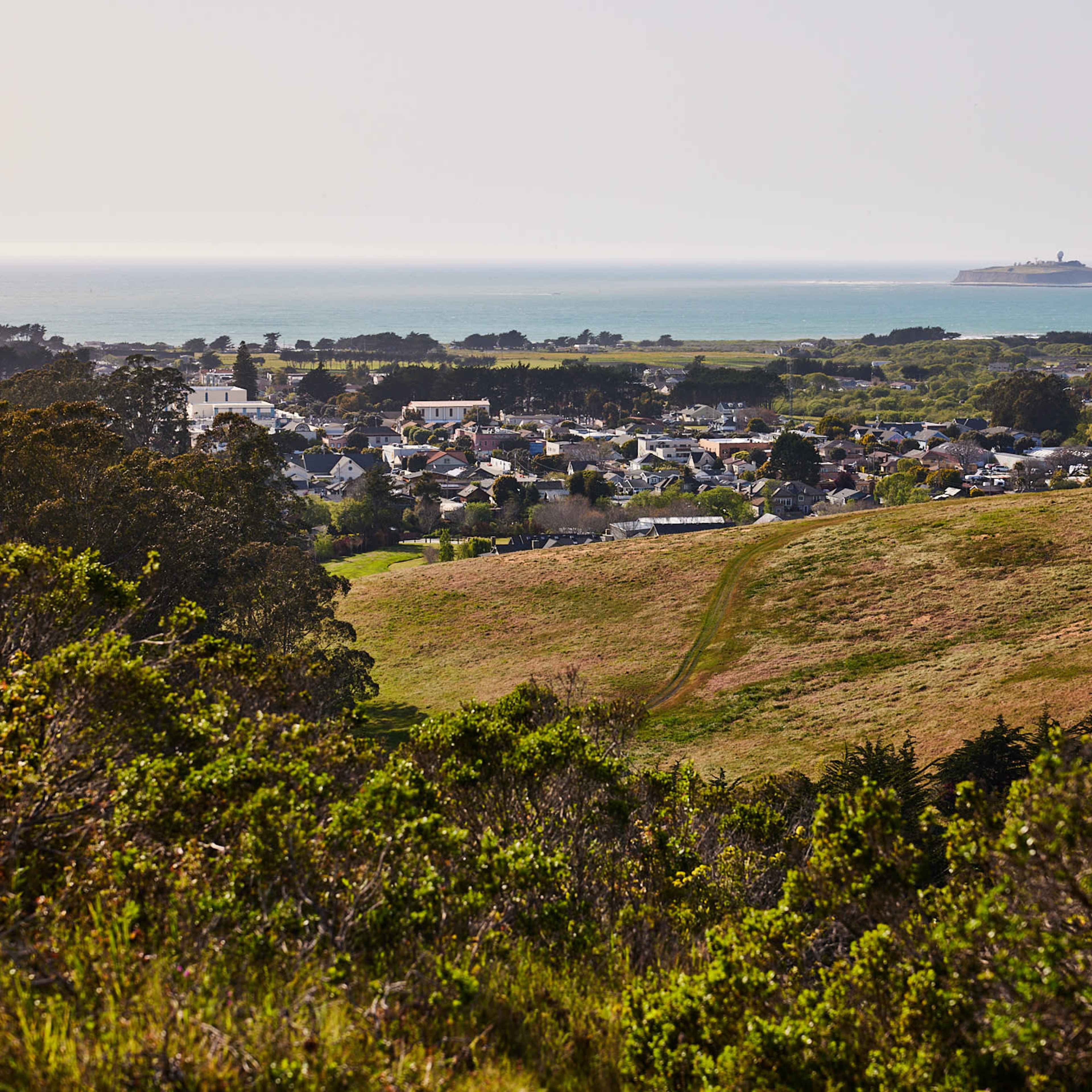 A coastal view with a small town nestled among green hills and the ocean in the background.