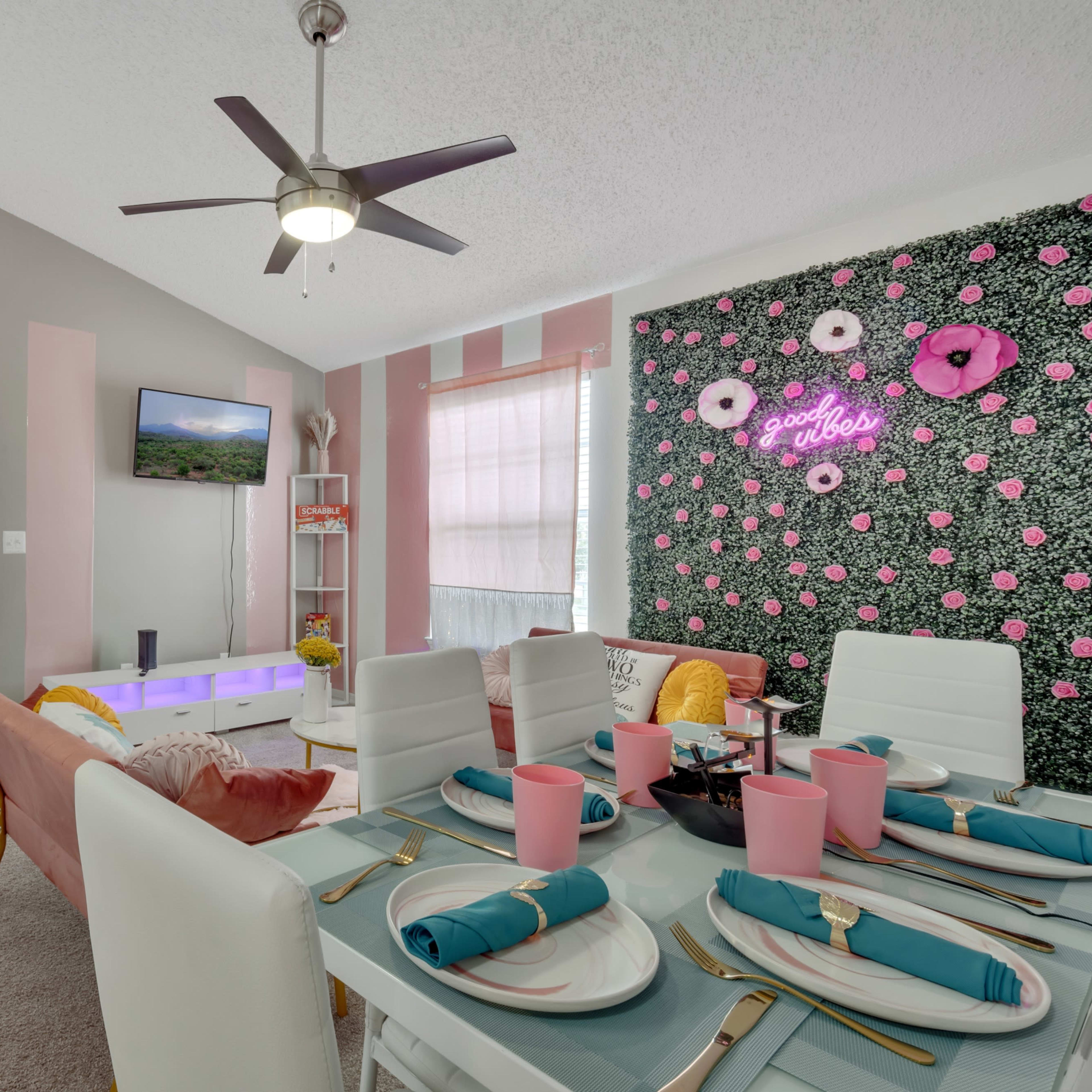 A modern dining area with a table set for a meal, featuring pink tableware and a wall adorned with floral decorations.