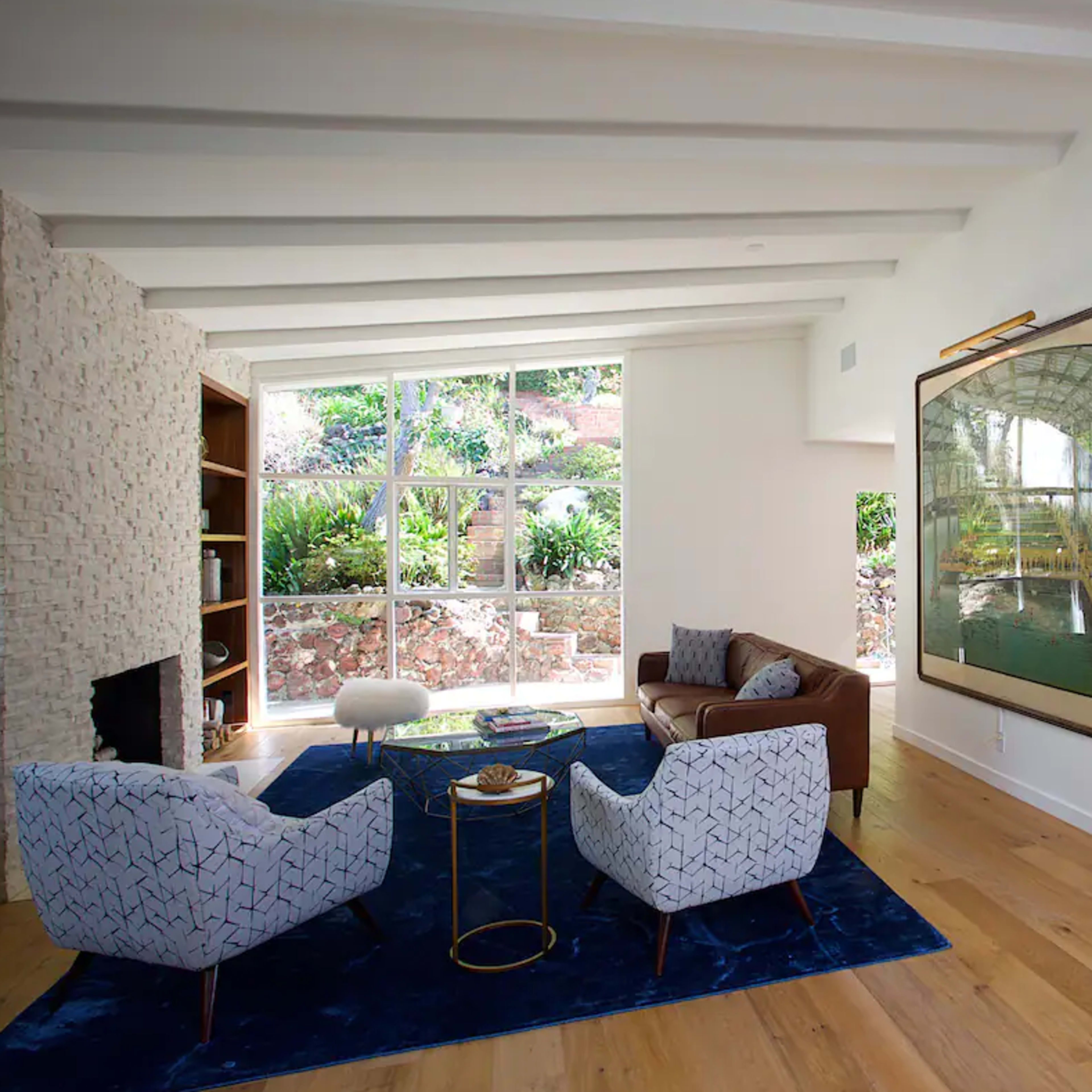 A modern living room with a sofa, armchairs, a coffee table, and large windows showcasing a garden outside.