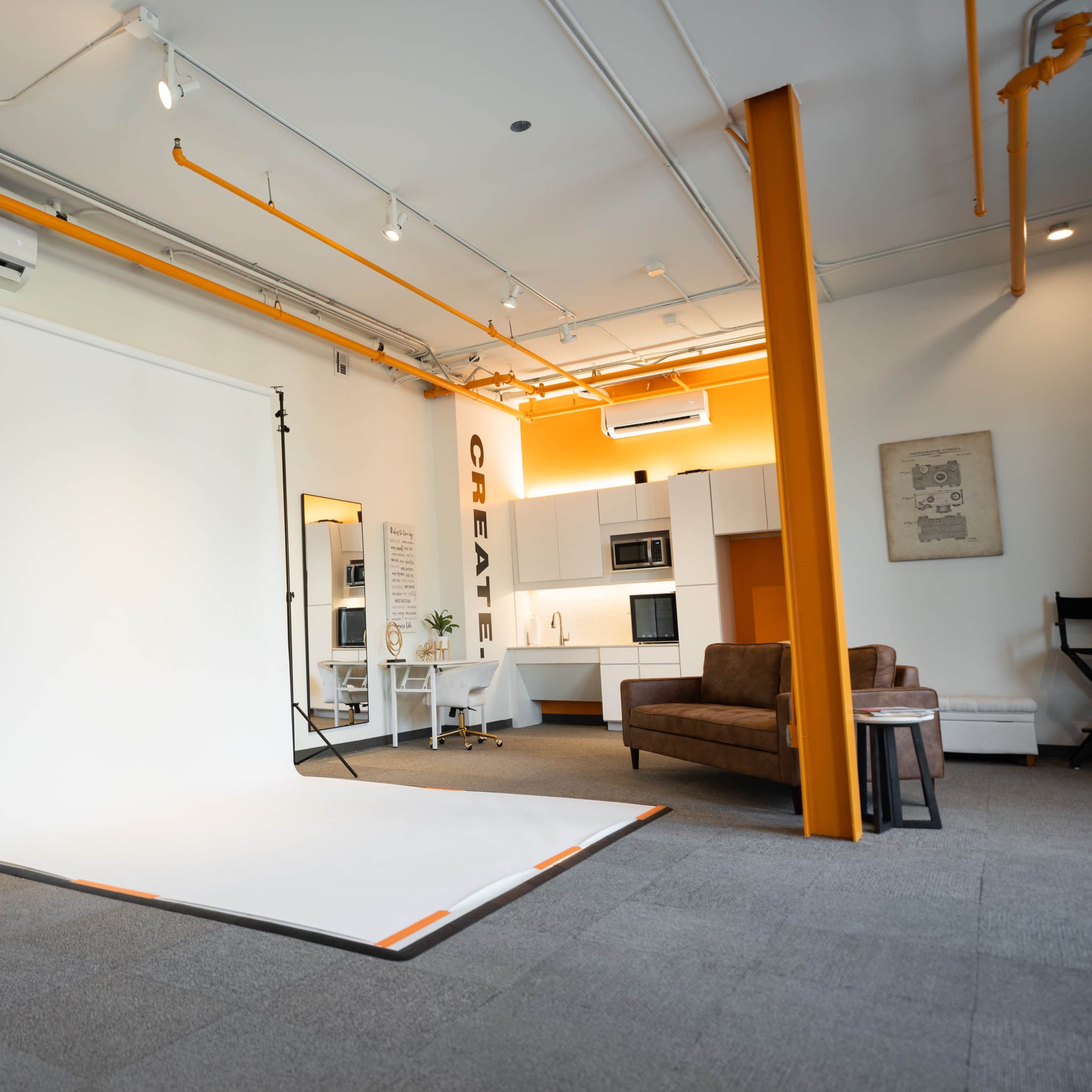 A spacious studio with a white backdrop, a brown couch, and a kitchenette in the background.