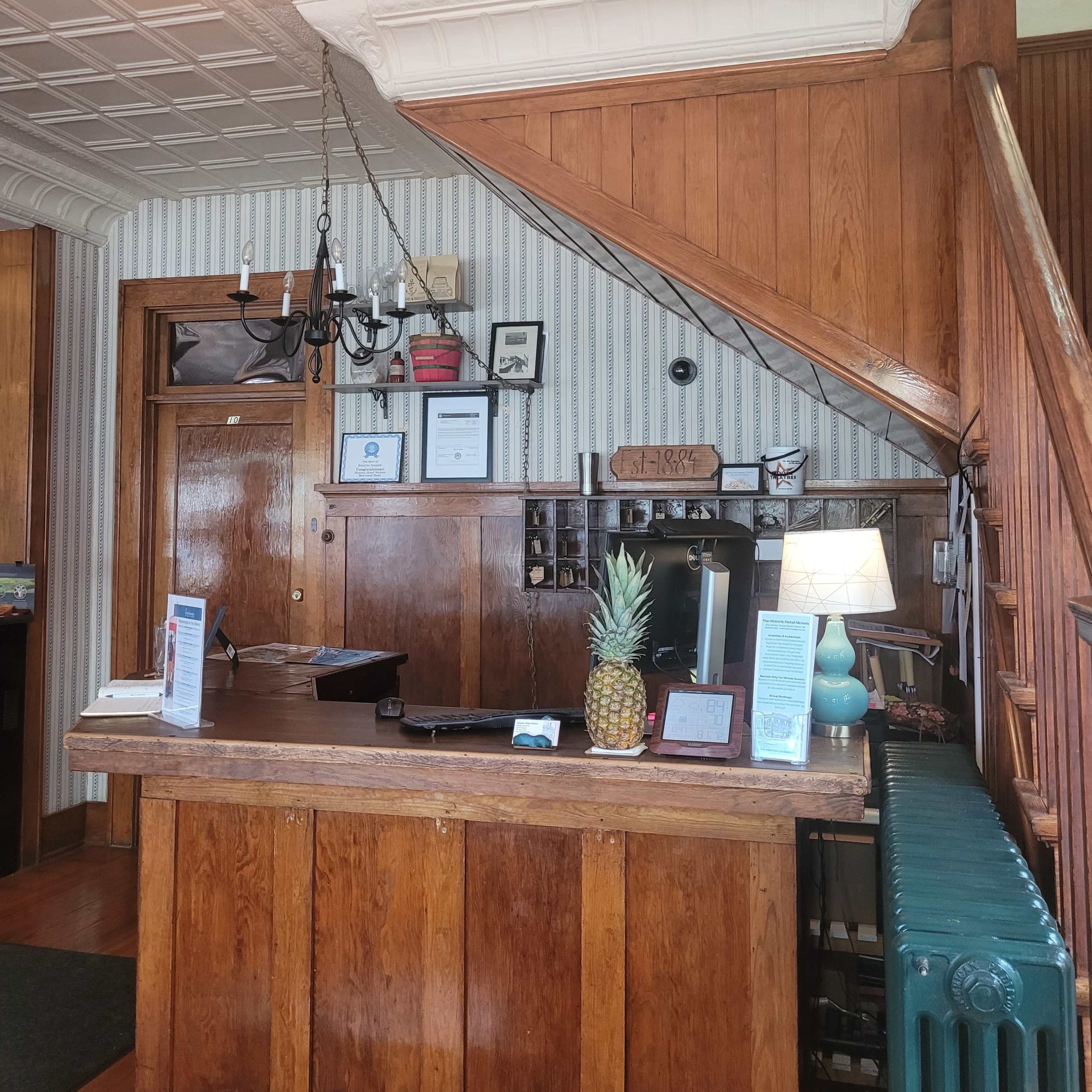 A wooden reception desk with a pineapple centerpiece, located in an area featuring a staircase and wall-mounted decor.