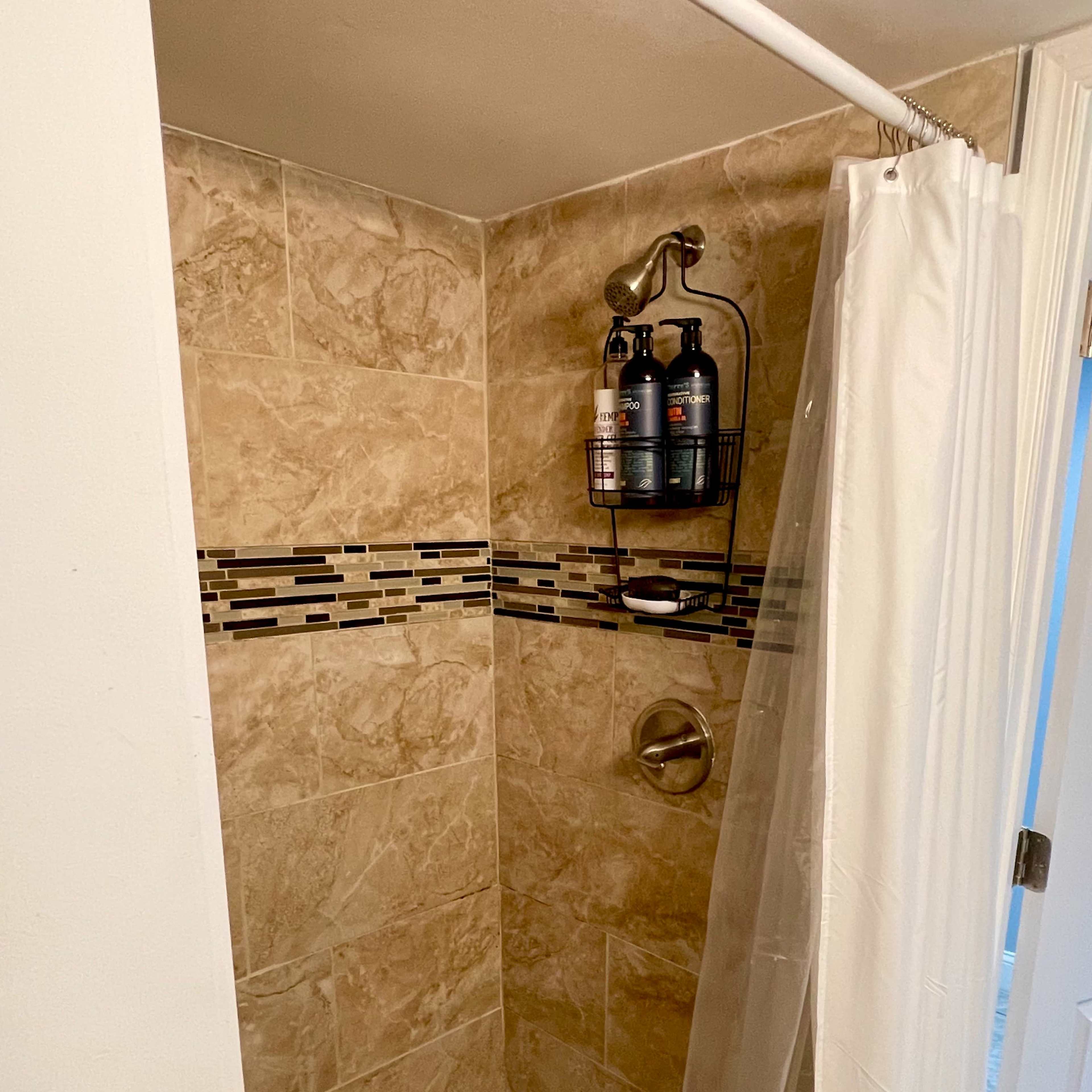 A tiled shower stall with a glass door, a showerhead, and shelves holding various bottles.