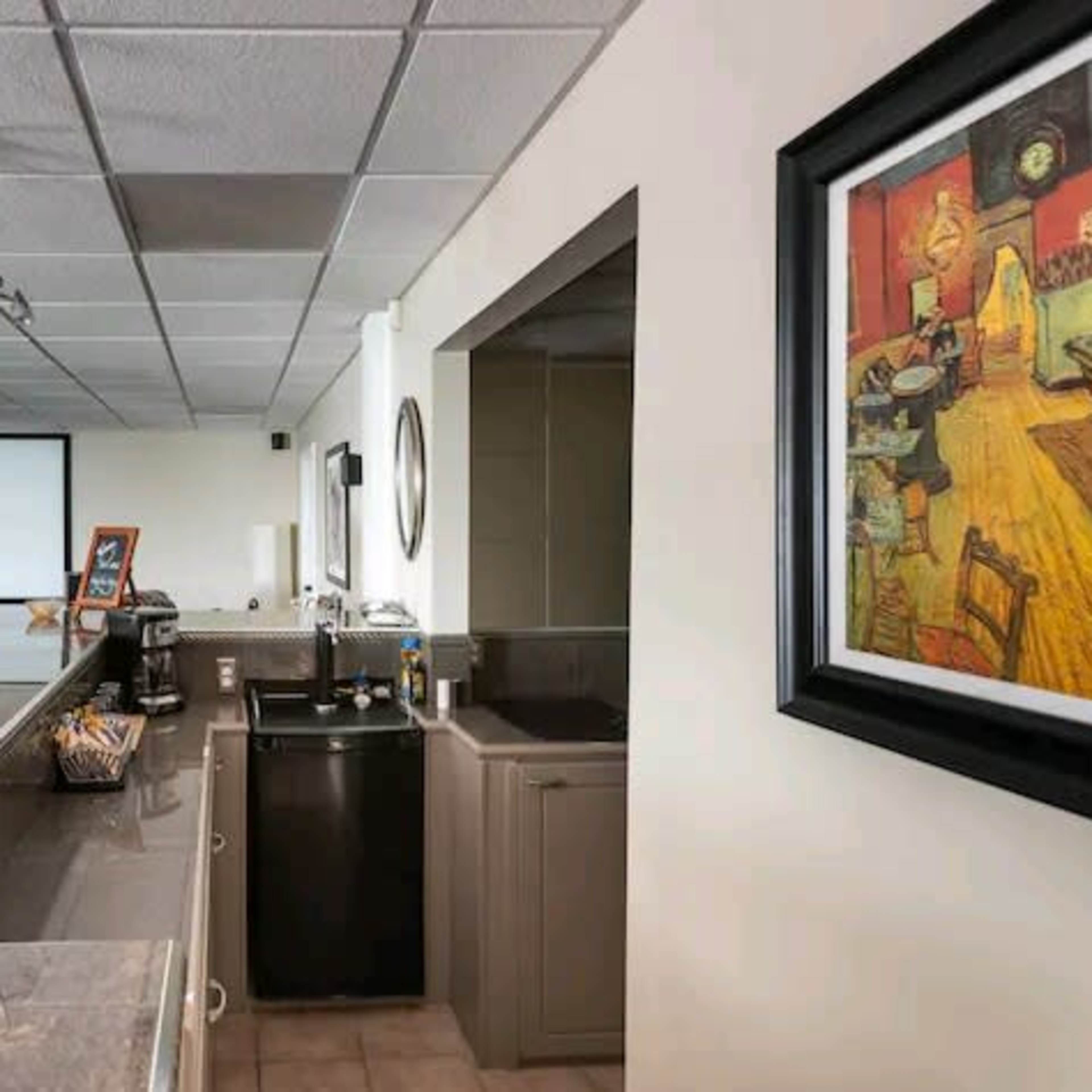A modern entertainment room with a countertop, sink, and a black fridge, featuring a projector screen and seating area in the background.