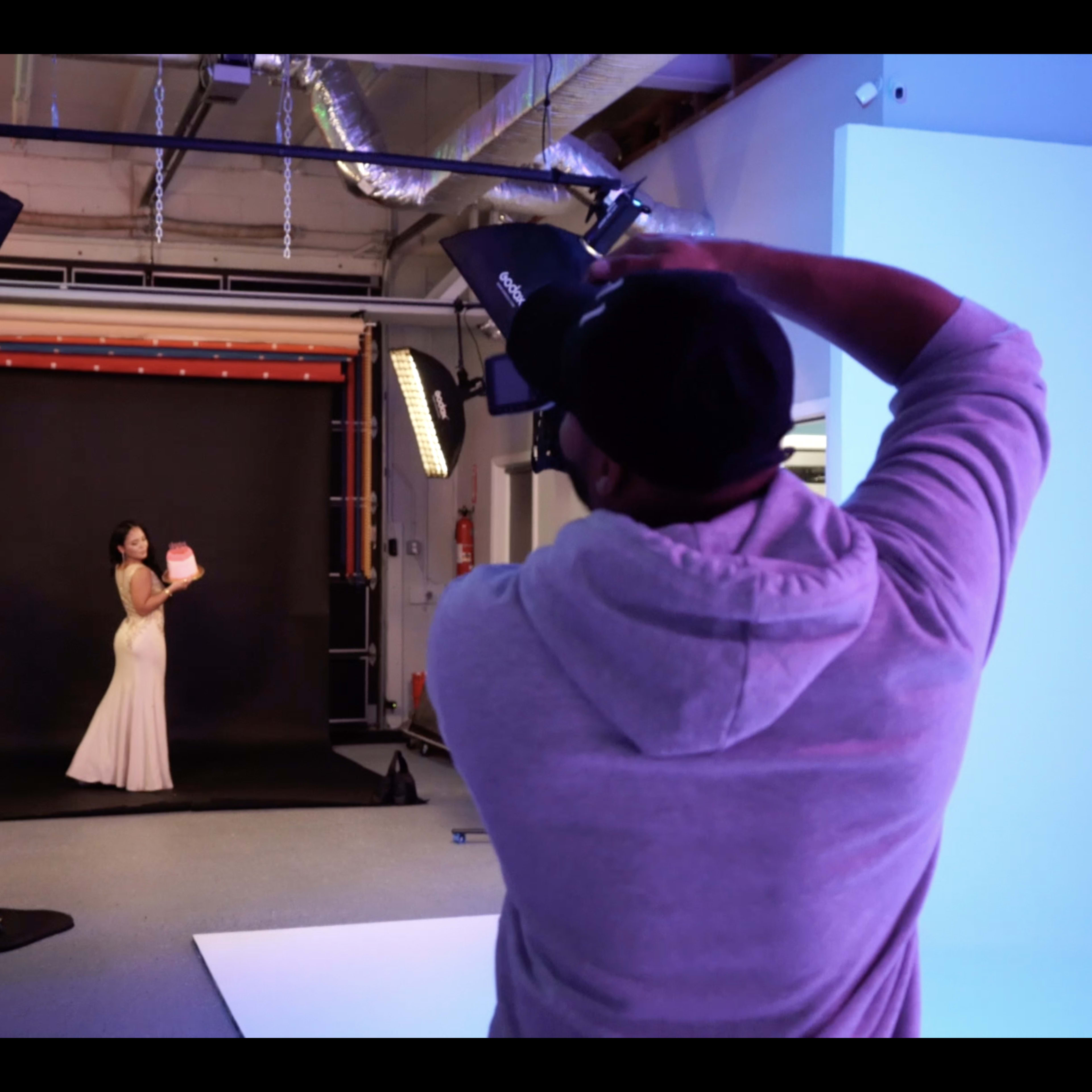 A photographer captures a model in a flowing dress against a black backdrop in a studio setting.