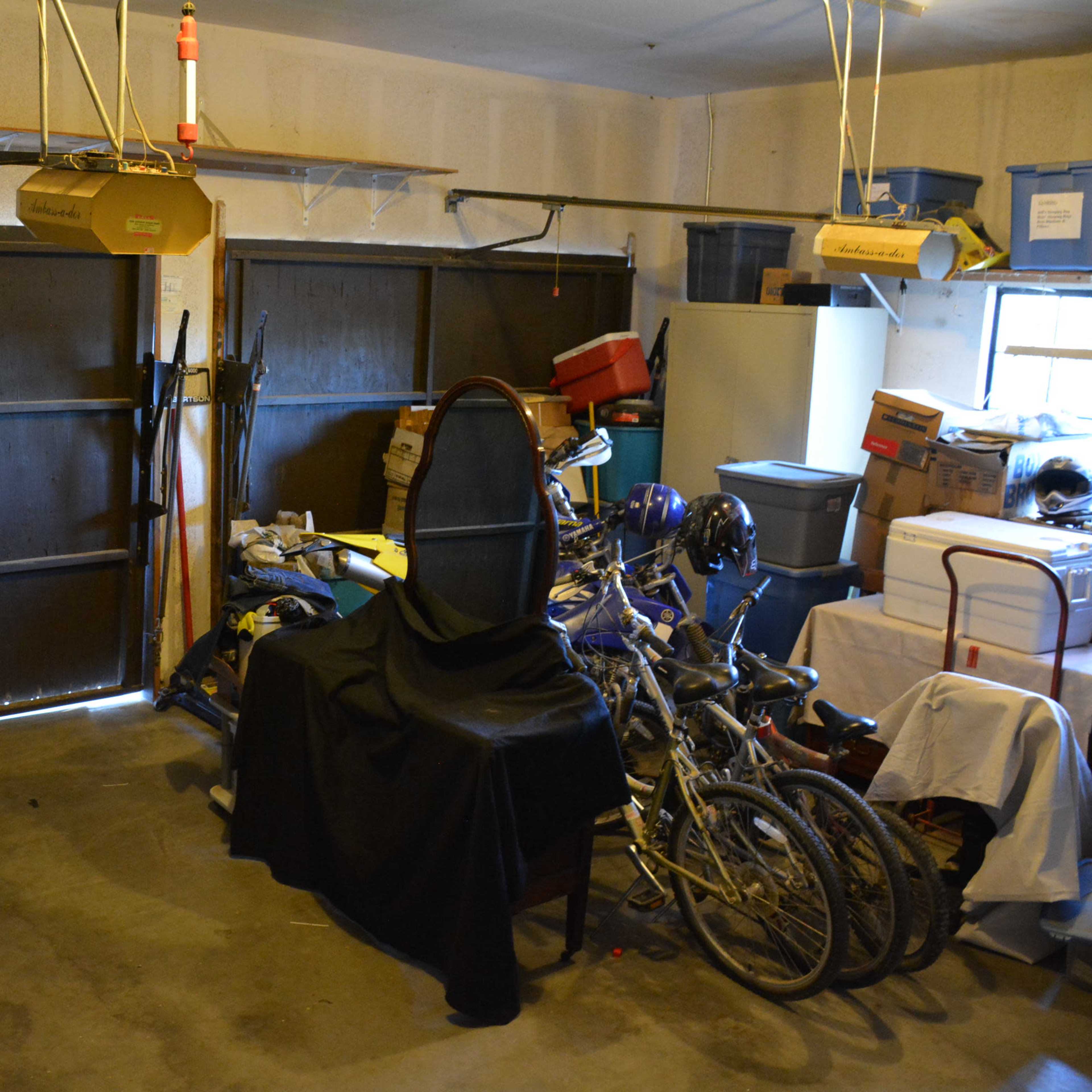 A cluttered garage contains various tools, bicycles, and storage boxes on shelves.