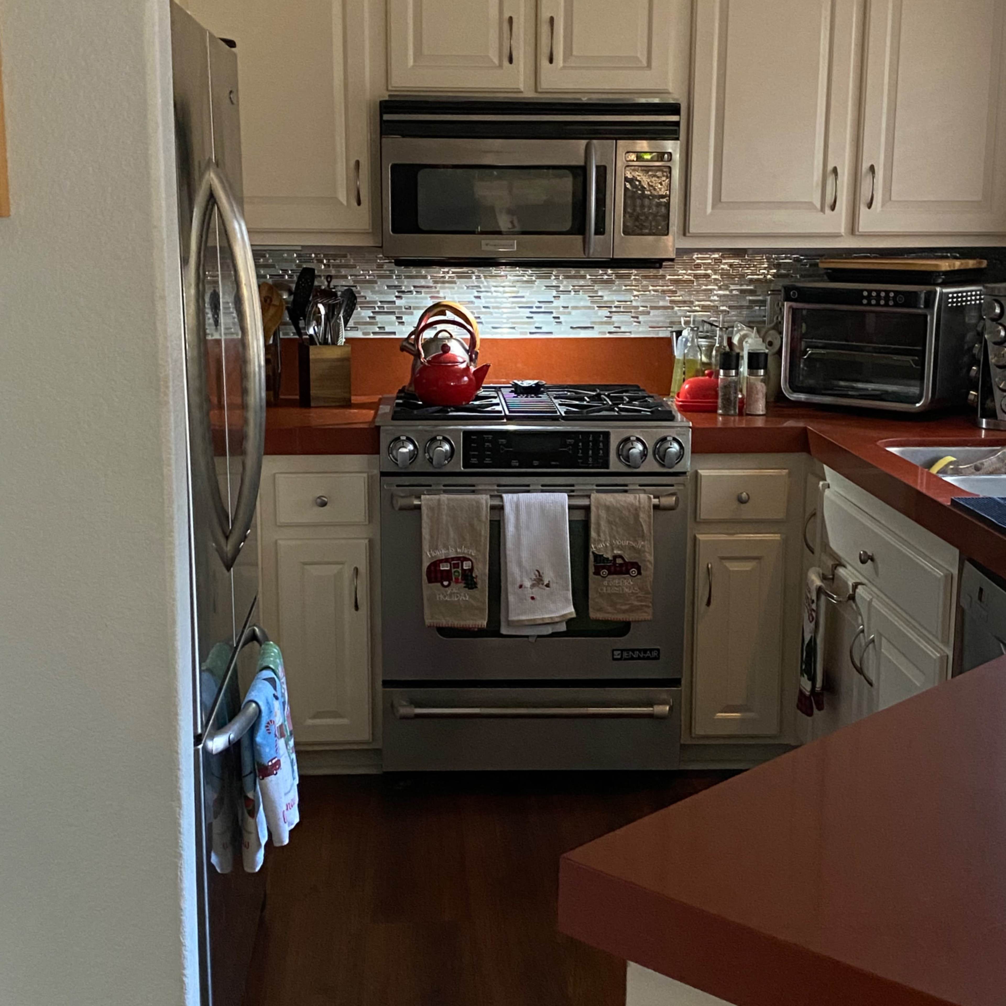 A kitchen featuring stainless steel appliances, including a gas stove and microwave, with red cookware and wooden countertops.
